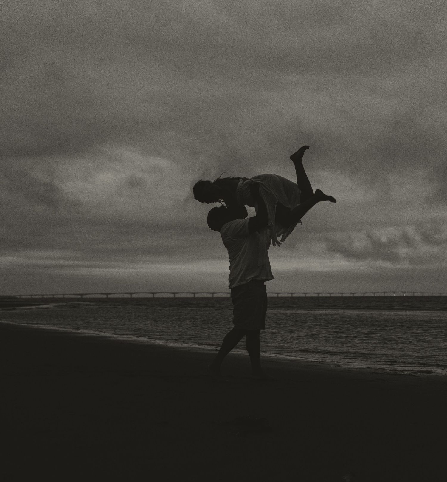 Silhouette of couple playfully lifting each other on beach at sunset.