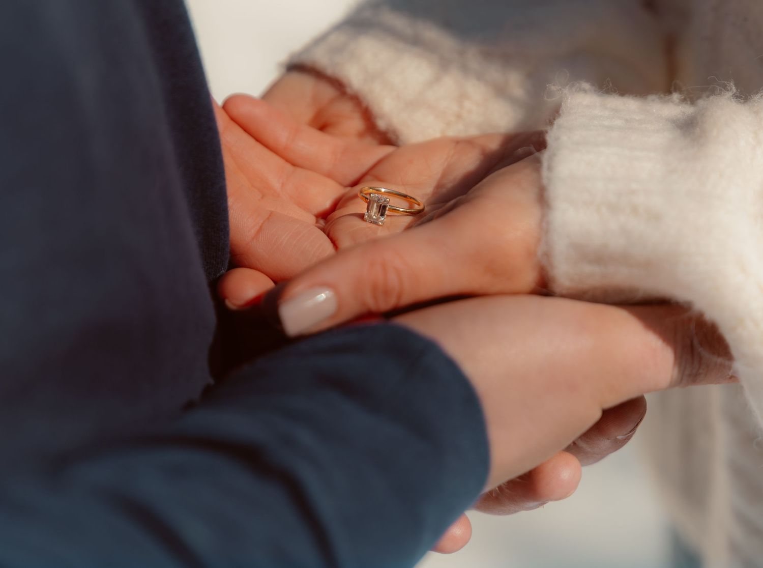 Close-up of hands holding each other with a gold ring visible, showing a tender romantic moment.
