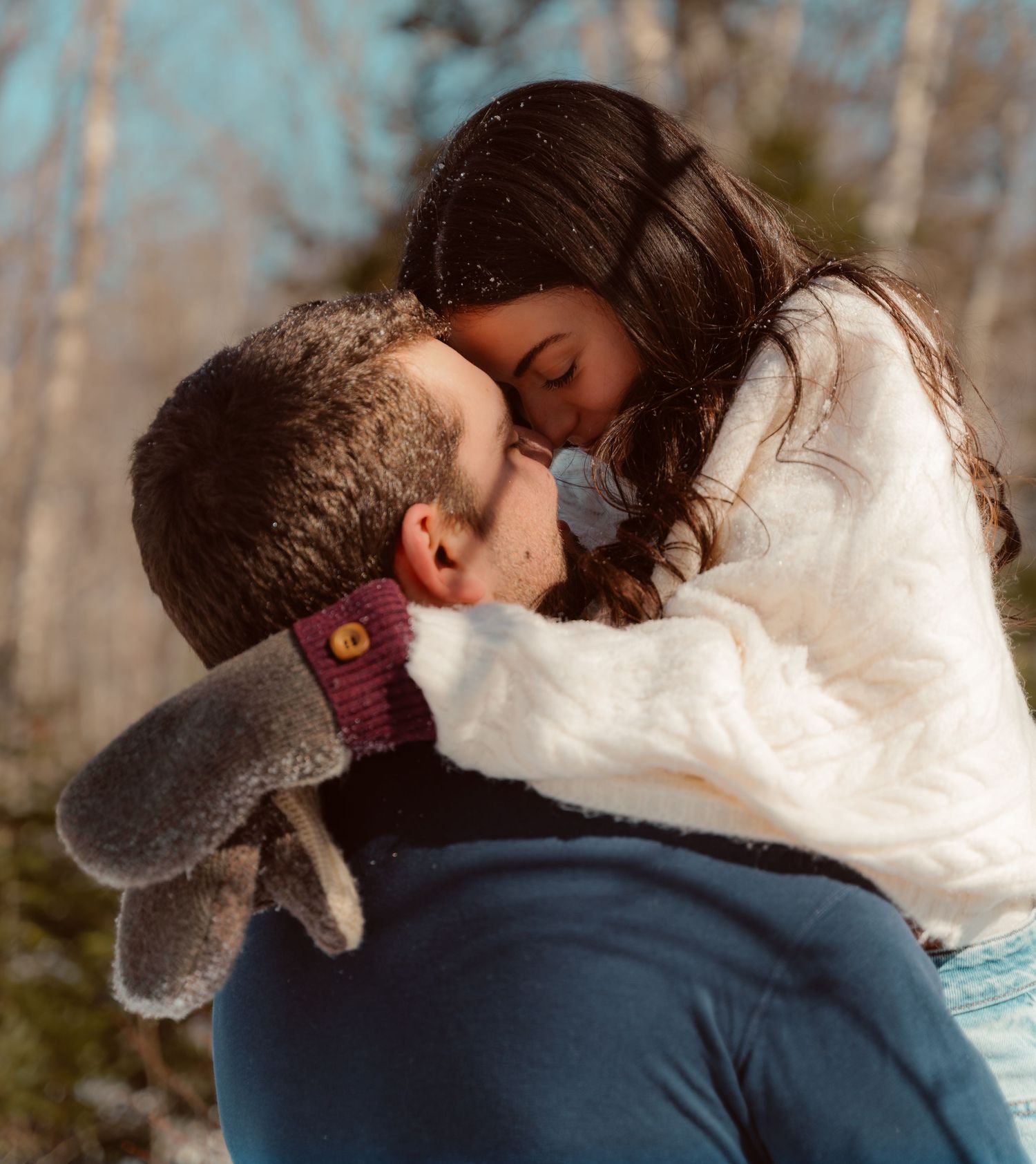 A romantic winter scene shows a couple sharing an intimate moment while holding a stuffed bunny toy in the snowy outdoors.