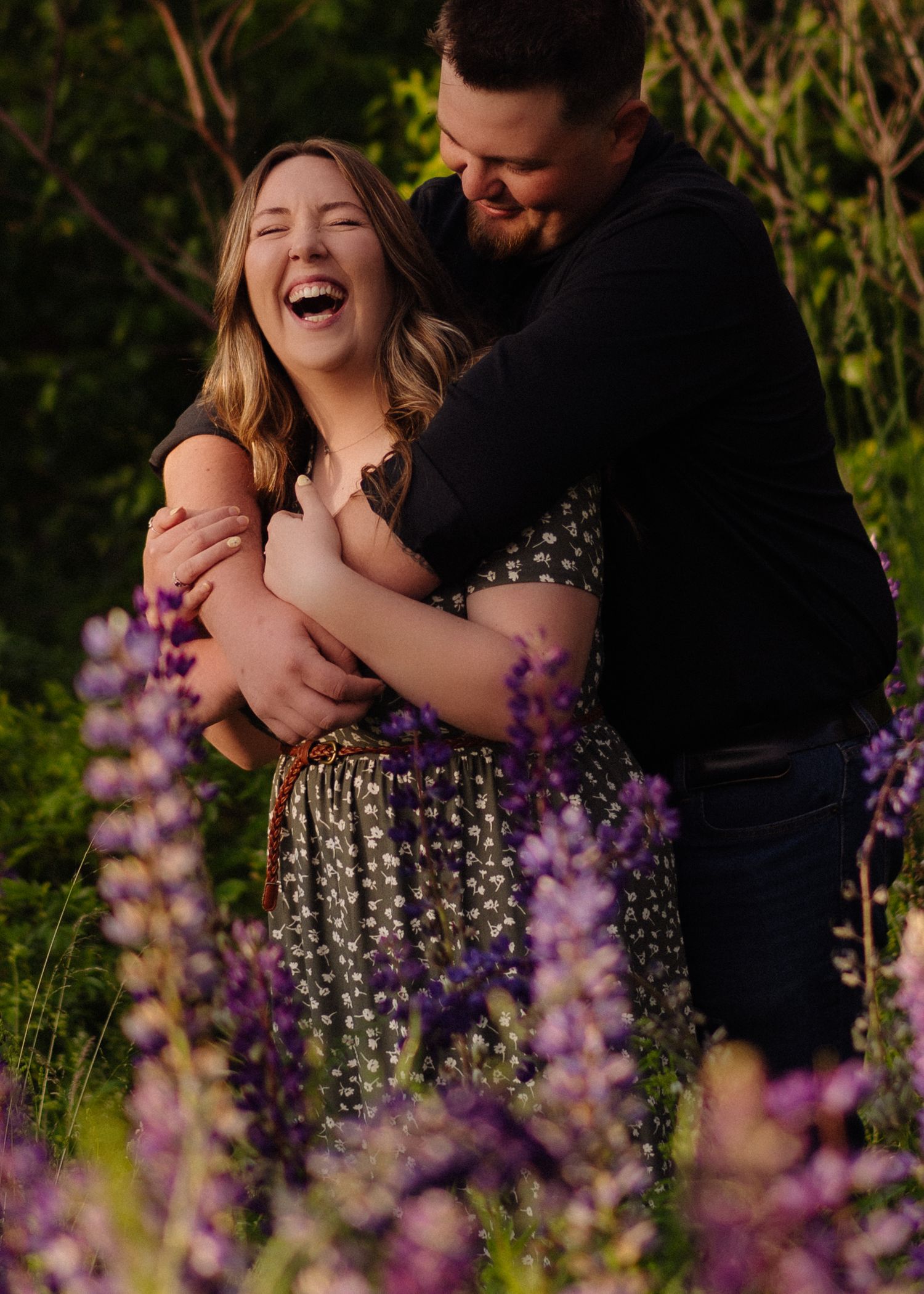 A couple shares joyful moments among blooming purple lupine flowers during a golden hour photoshoot.