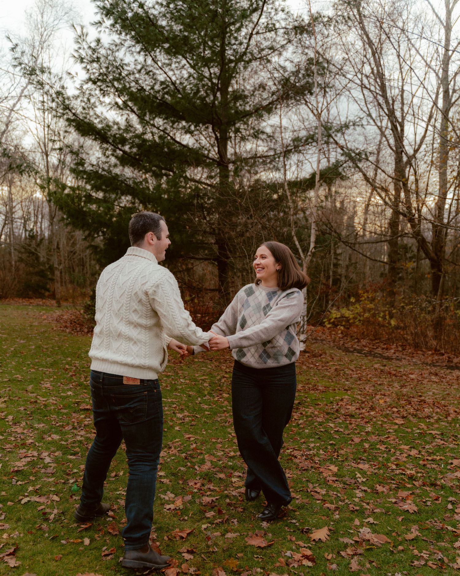 A joyful couple dancing together in a rustic outdoor setting with fall leaves on the ground.