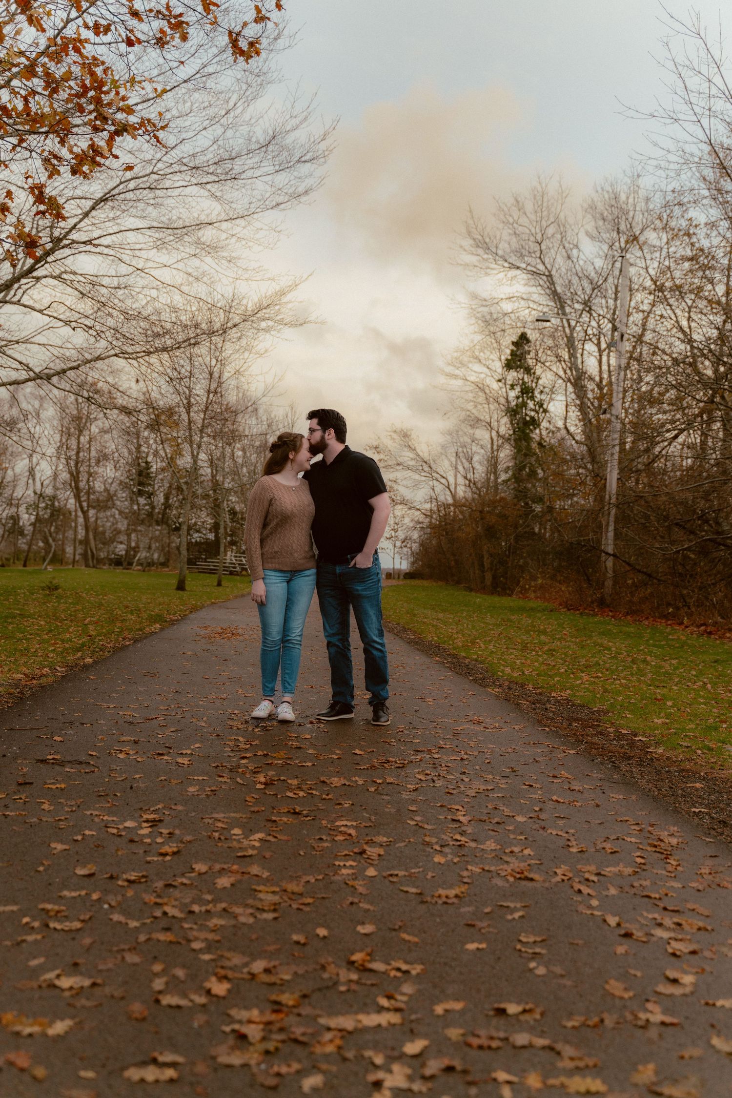 A couple walks together on a leaf-covered path through an autumn park during golden hour.
