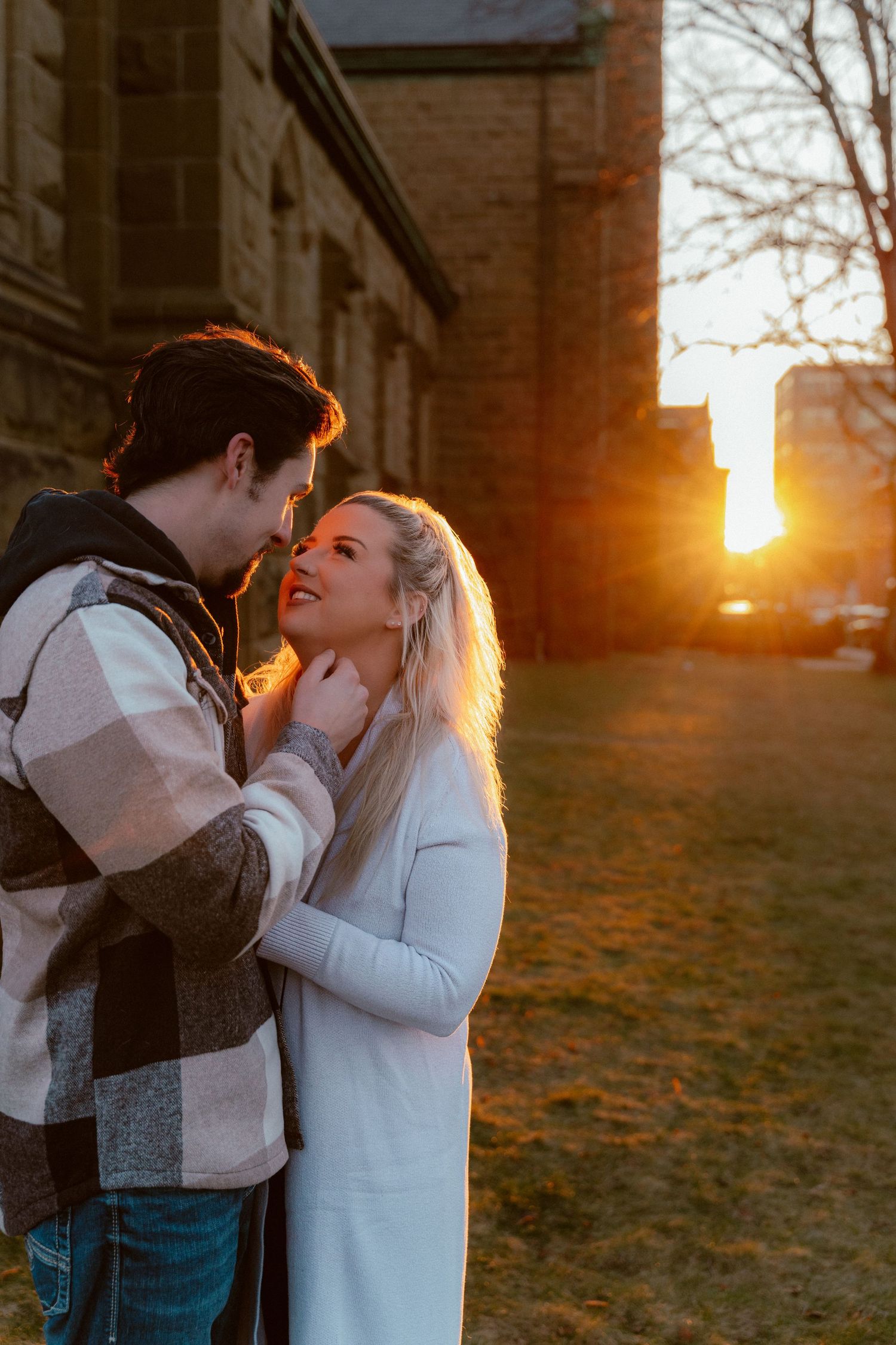 Romantic couple sharing intimate moment at sunset with brick building backdrop.