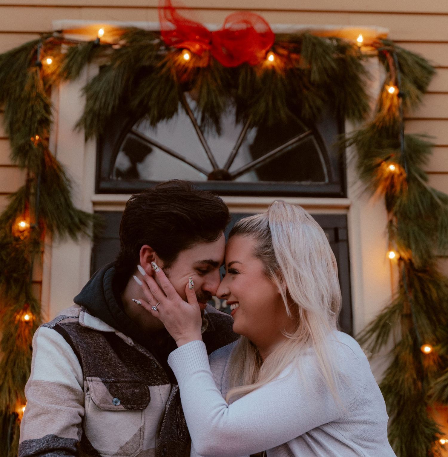 A romantic moment under holiday greenery and lights adorning a doorway.