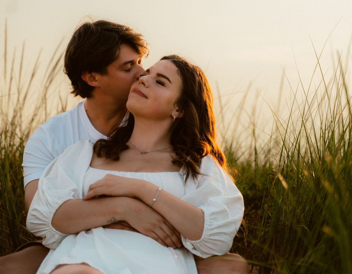 Tender embrace in golden sunlit meadow with tall grass swaying in background.