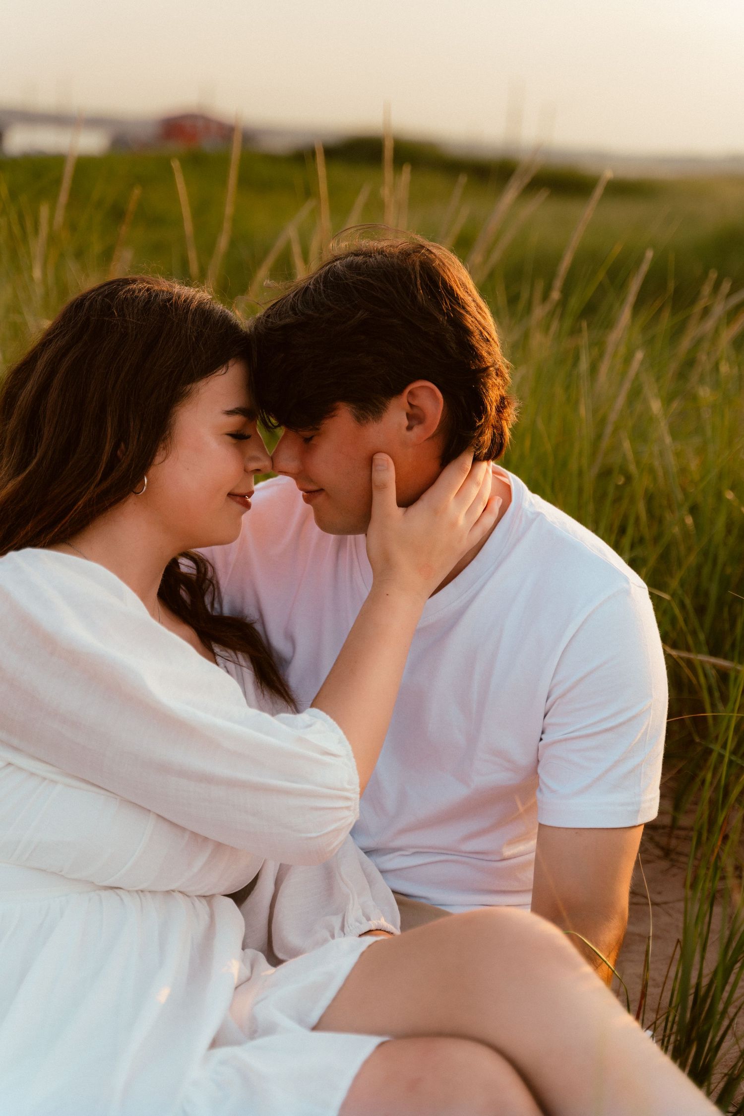 Intimate couple sharing tender moment in sunlit field of tall grass.