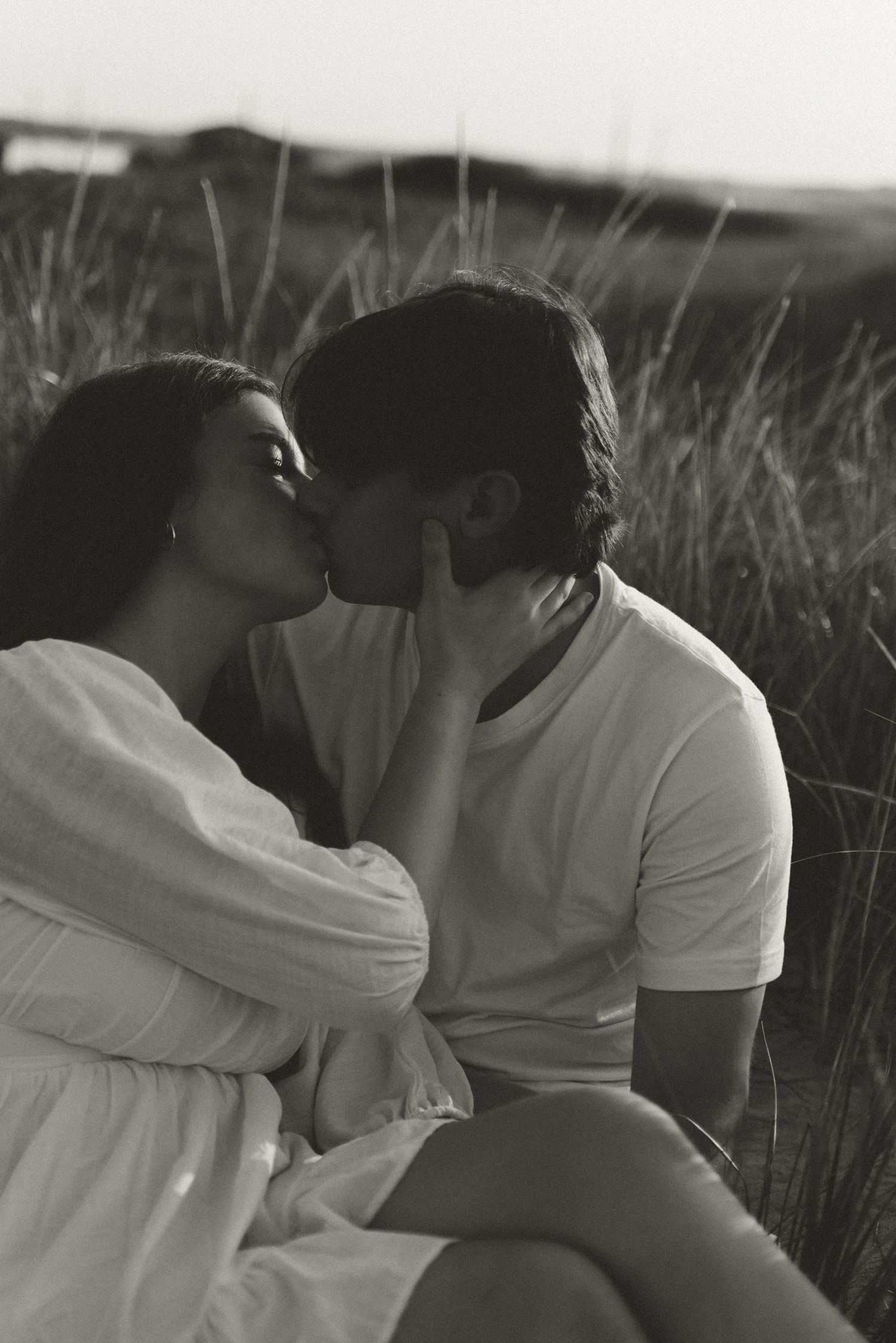 Black and white portrait of couple sharing intimate moment in tall grass.
