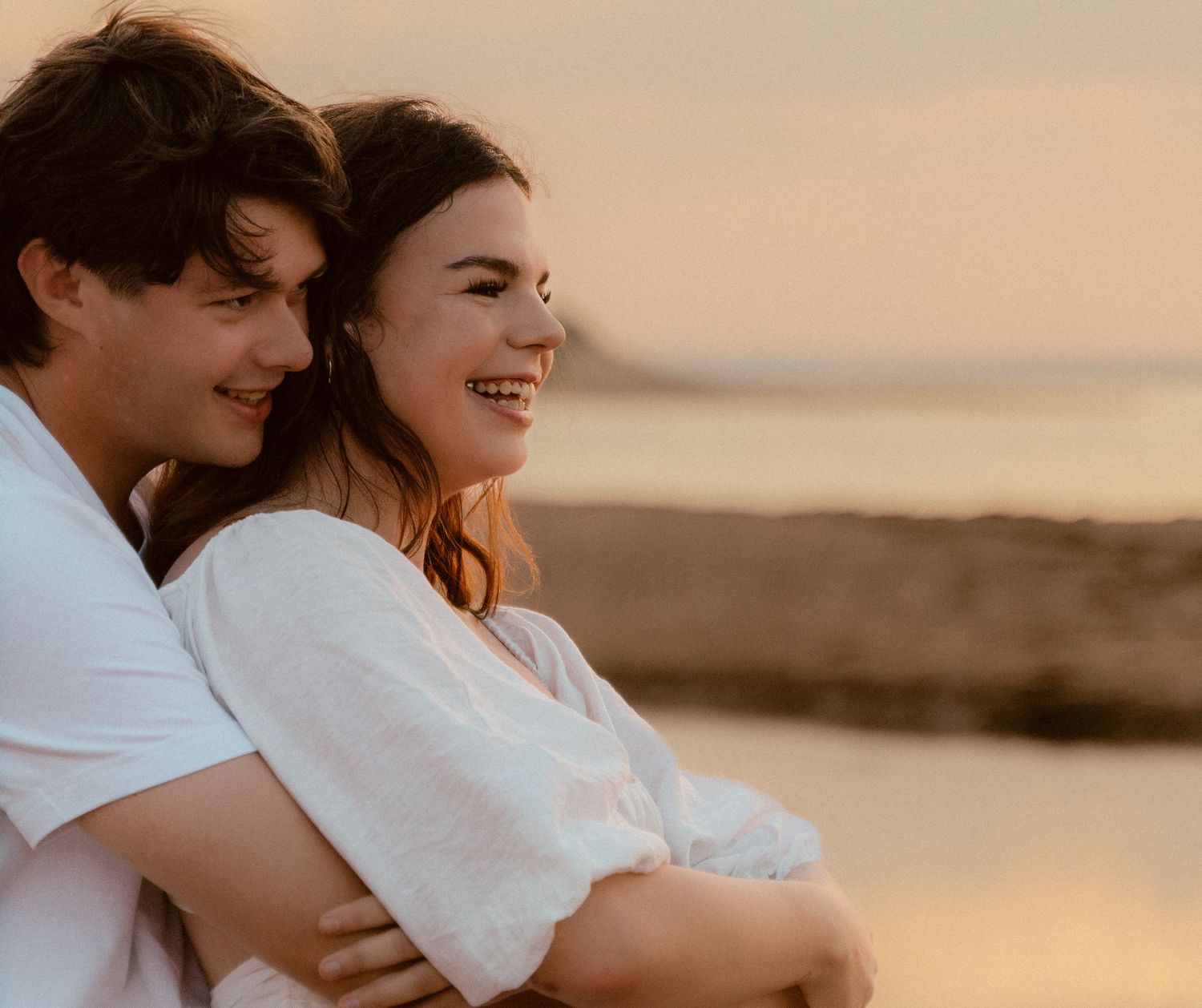 Joyful couple embracing on beach during golden hour sunset.