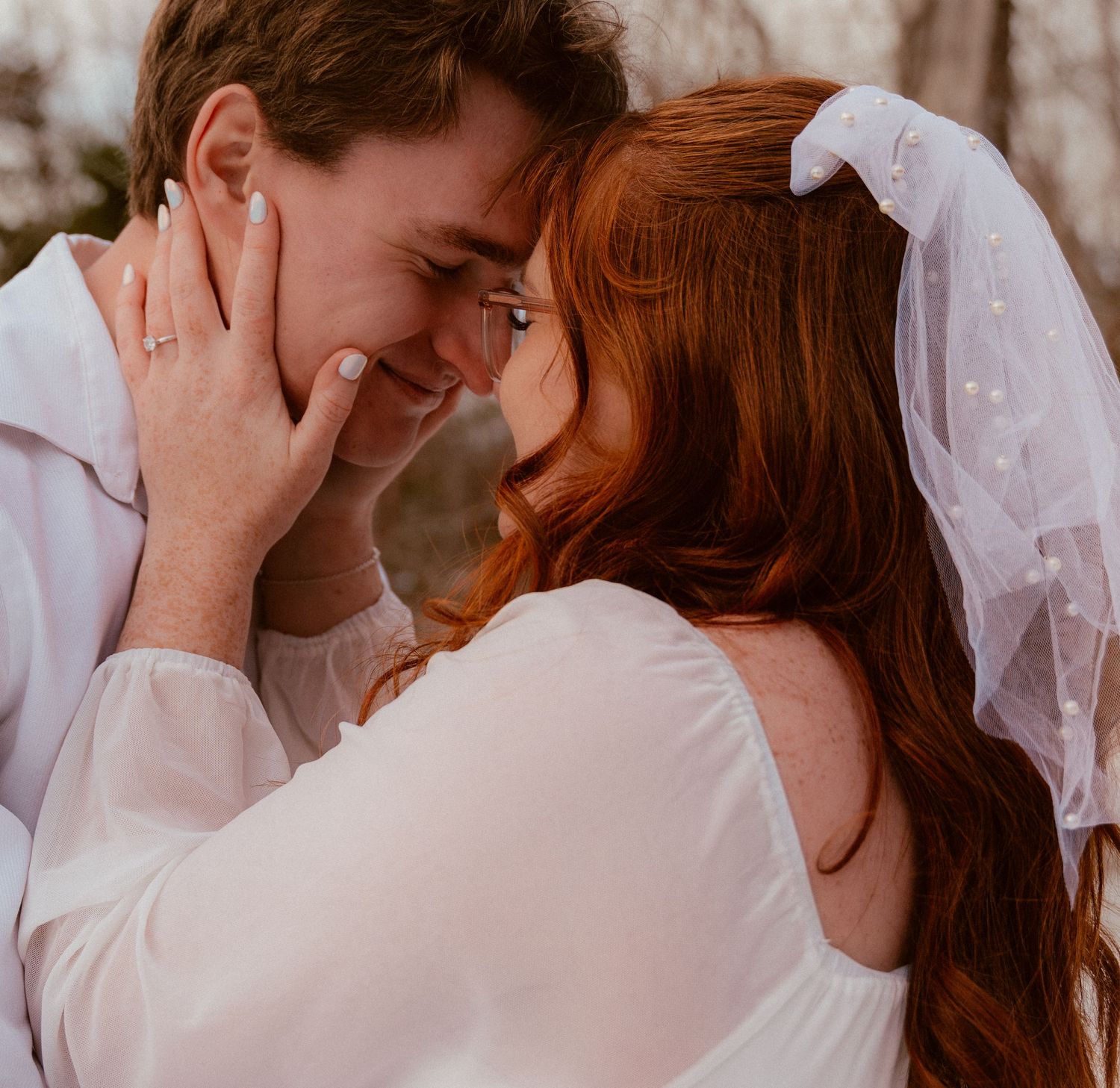 A romantic moment captured in soft light as a couple in white attire share an intimate embrace with gentle laughter.
