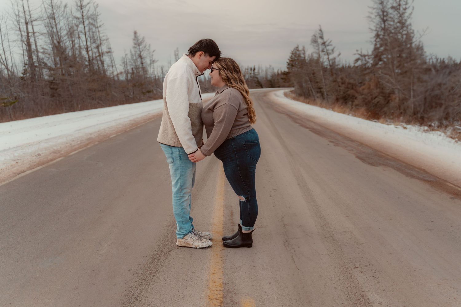 A loving couple embraces in the middle of an empty rural road surrounded by winter trees on a misty day.