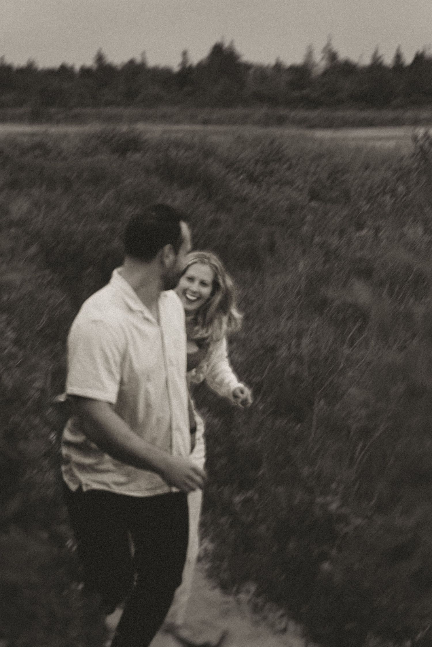A couple shares an intimate moment together in a grassy field on a cloudy day.