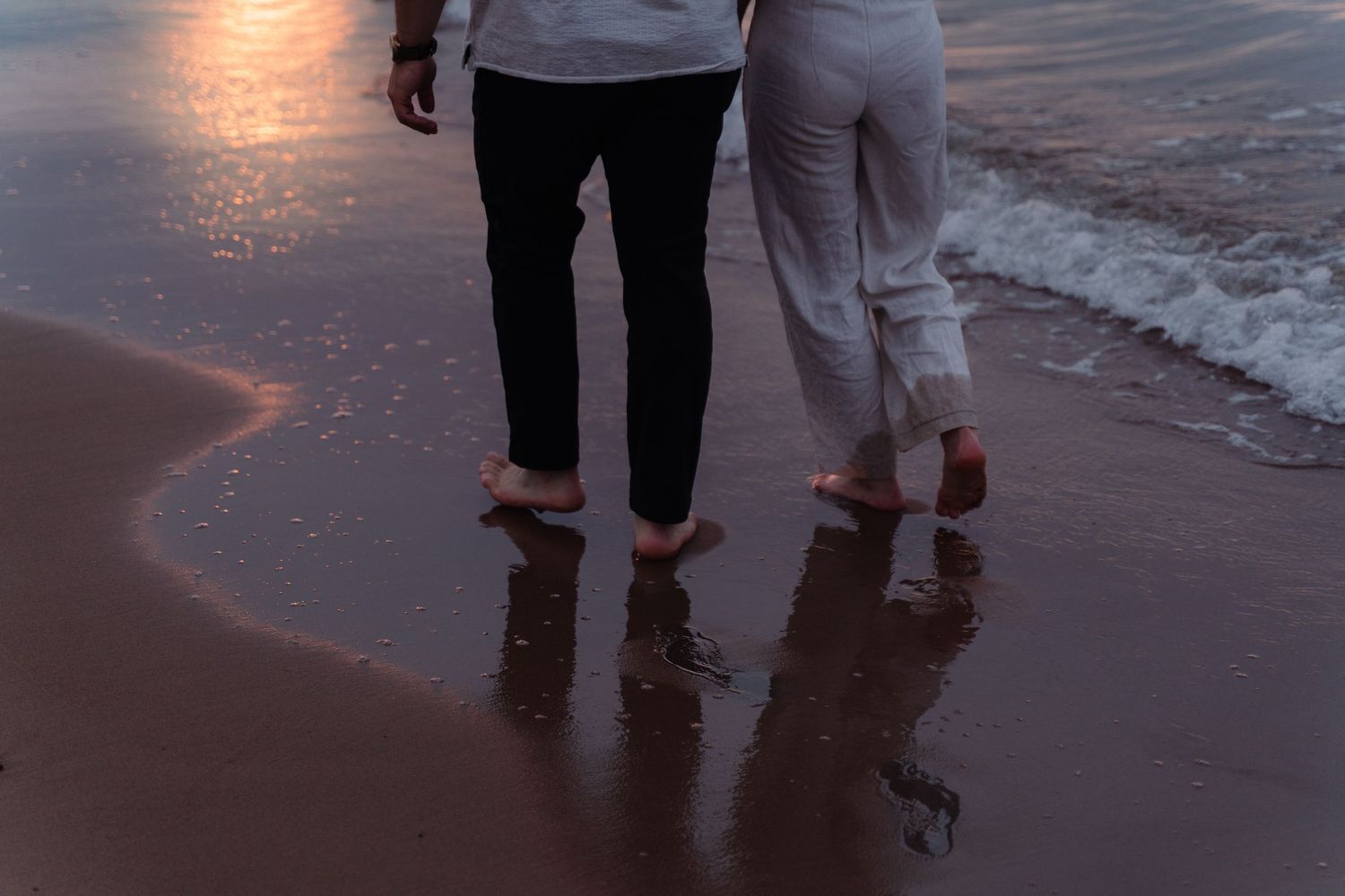 People walking along a beach at sunset with their feet in the shallow water.