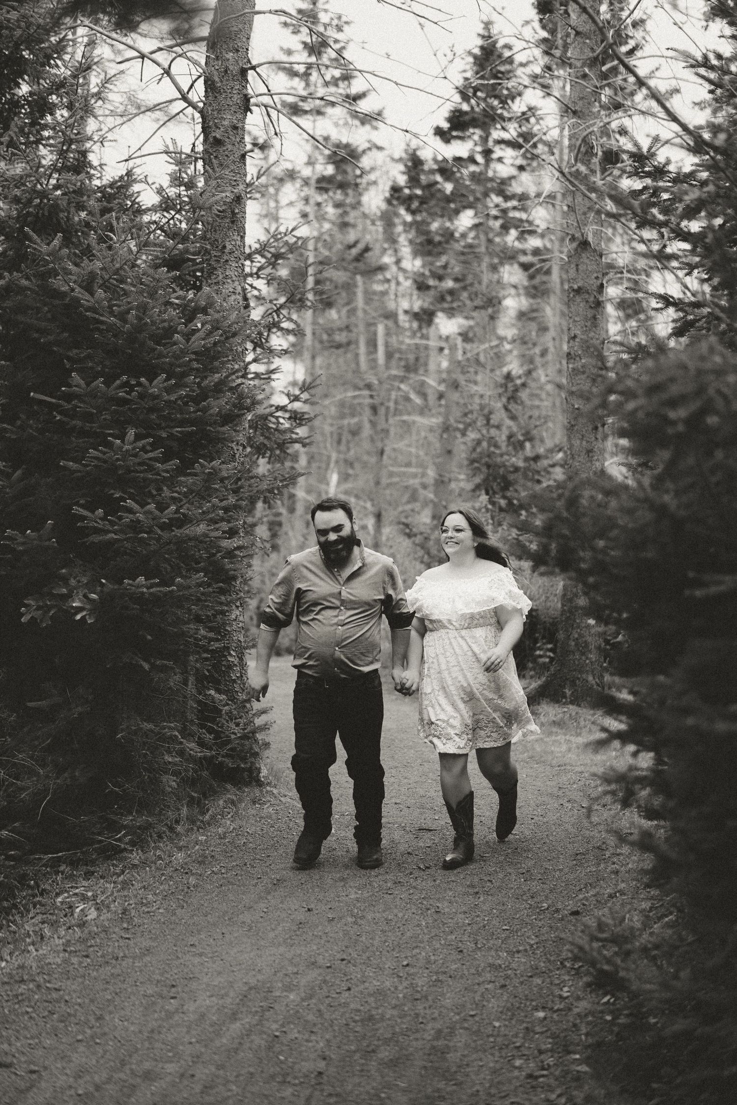 A couple runs joyfully through a wooded forest path in black and white photography.