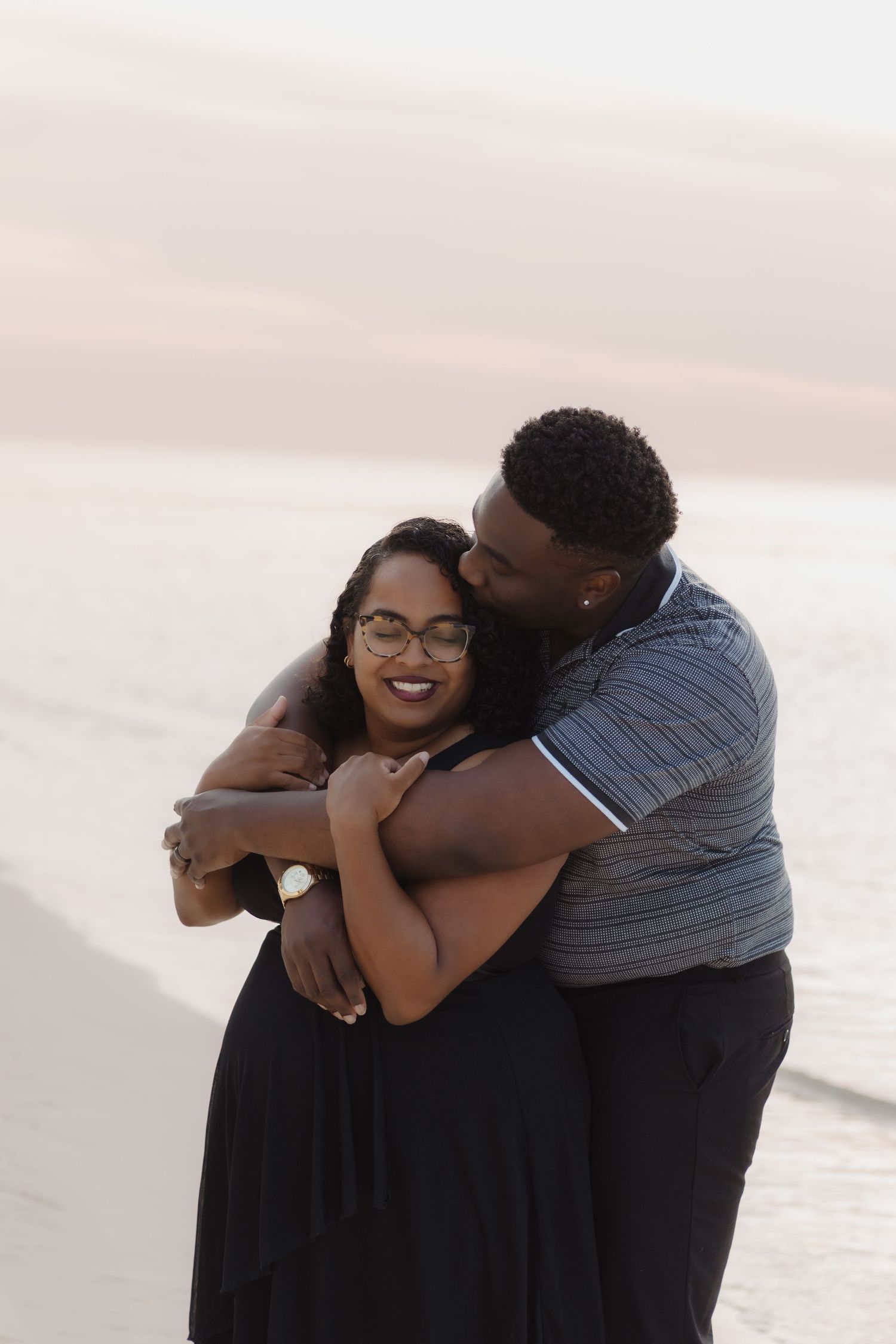 A joyful couple shares a loving embrace while laughing together on a sunset beach.