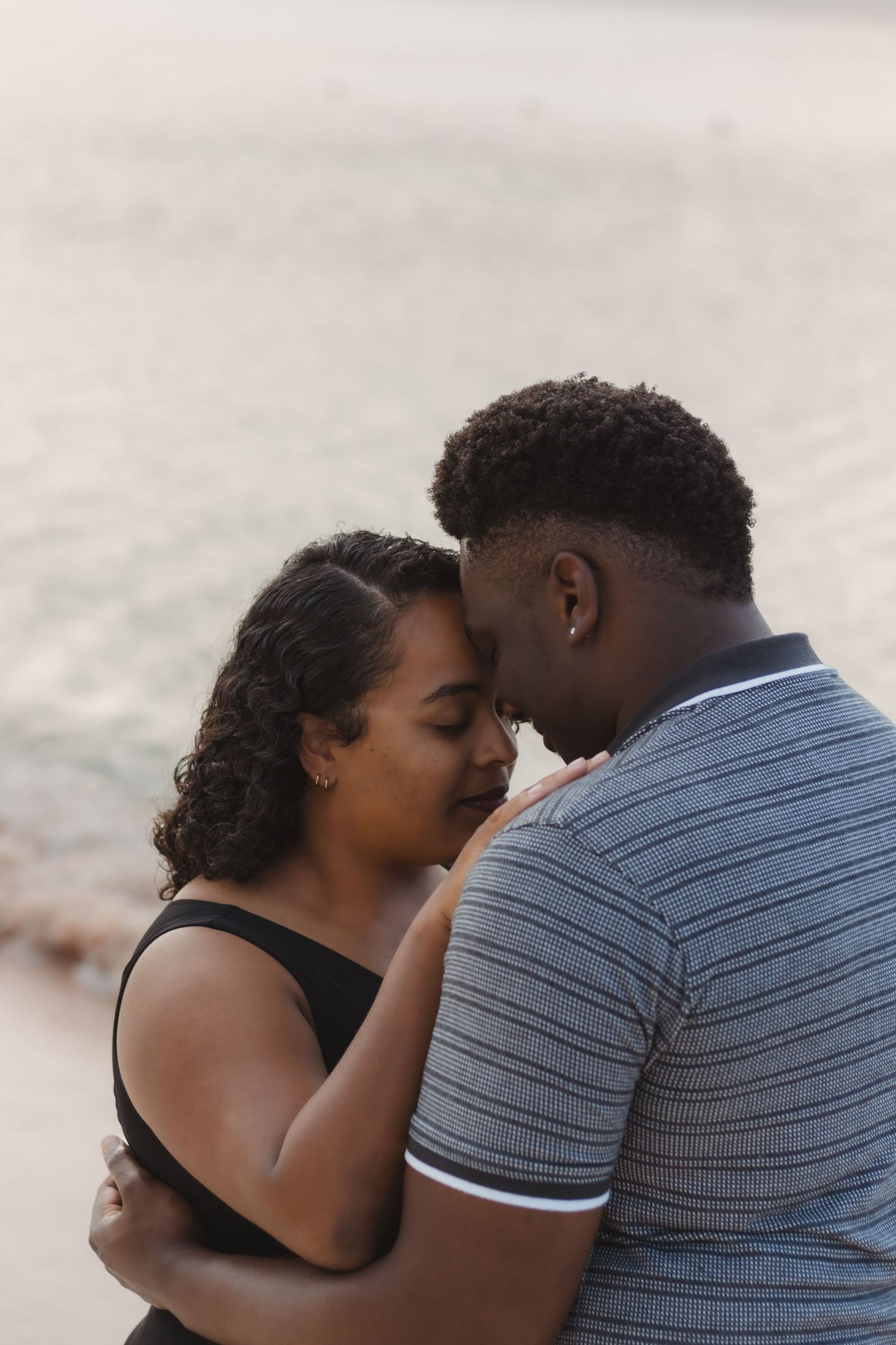A tender moment between a couple in casual attire sharing an intimate embrace on the beach.