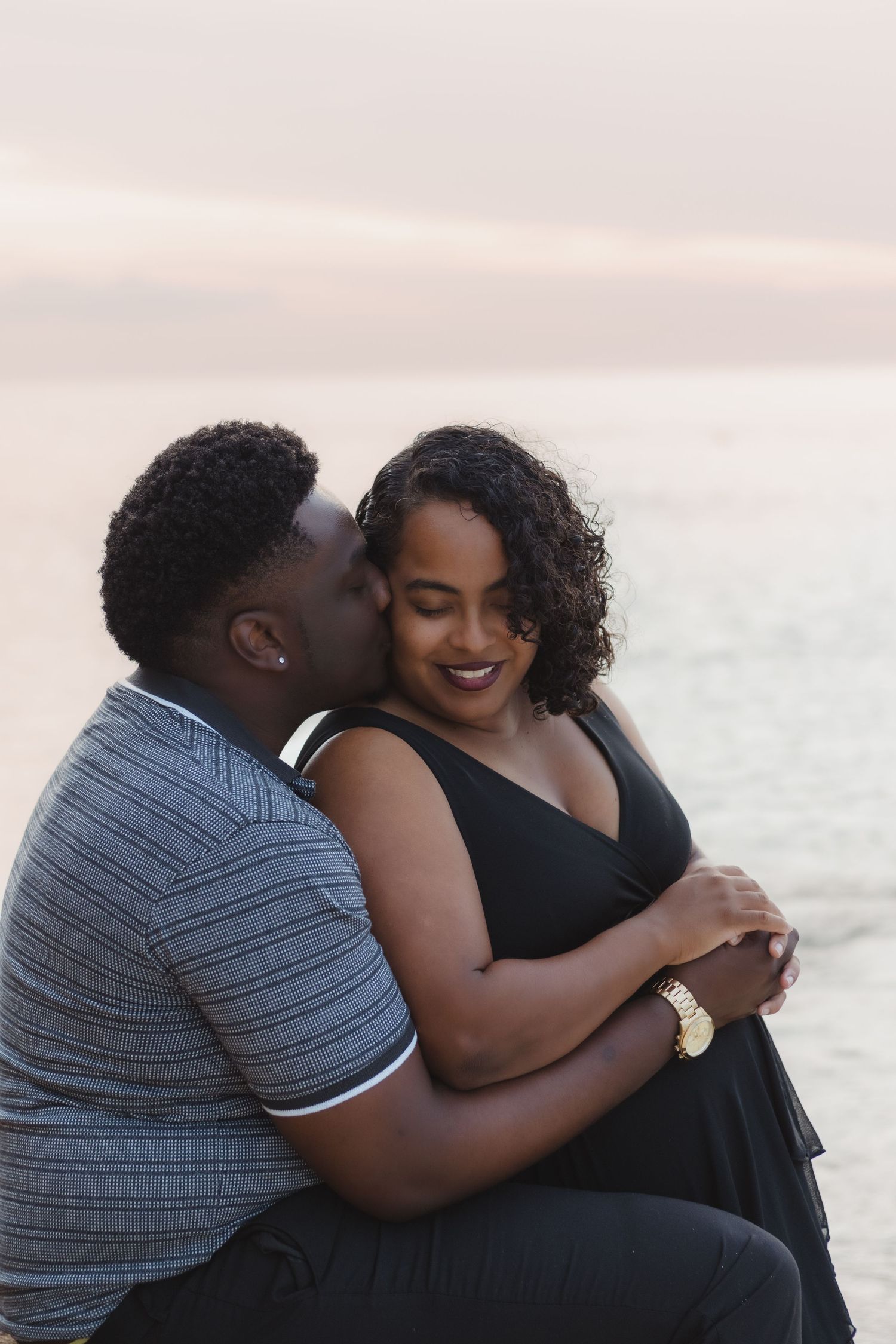 An affectionate couple shares a tender moment on the beach during golden hour.