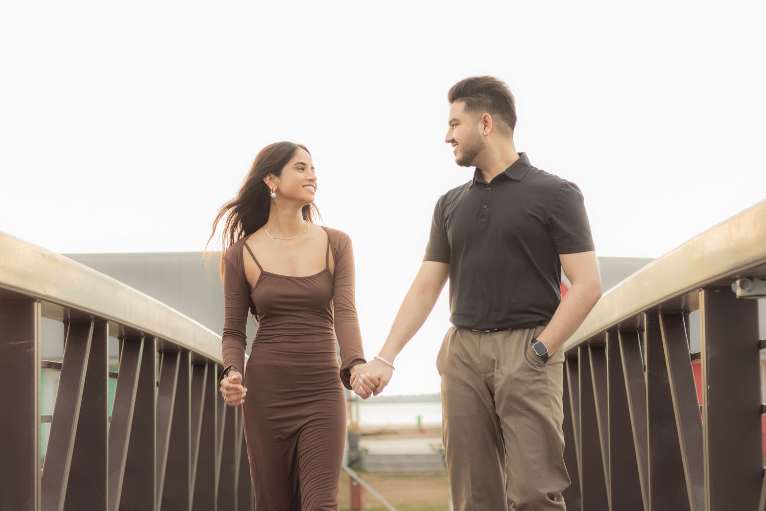 Couple holds hands while walking together on a wooden bridge during golden hour.