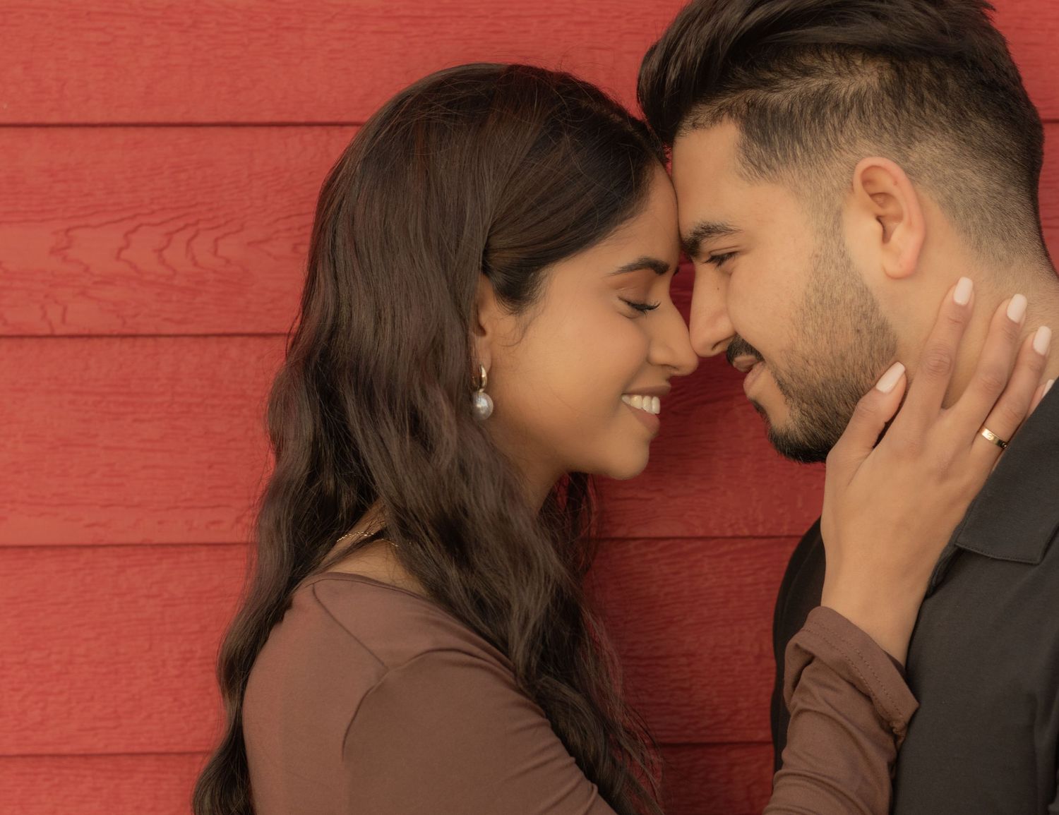 Romantic couple shares an intimate moment against a red wooden wall background.
