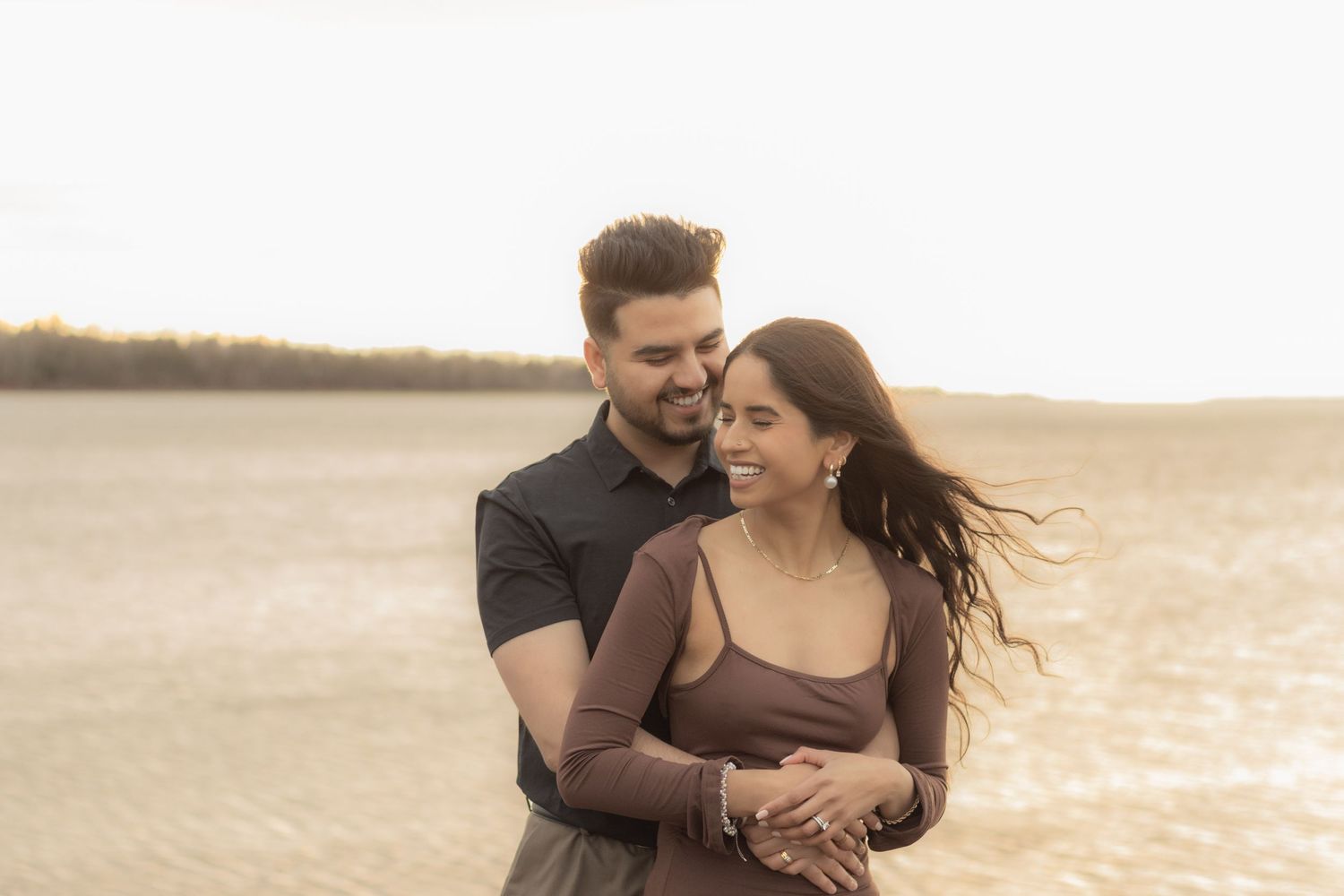Couple embracing on a beach during golden hour with windswept hair.