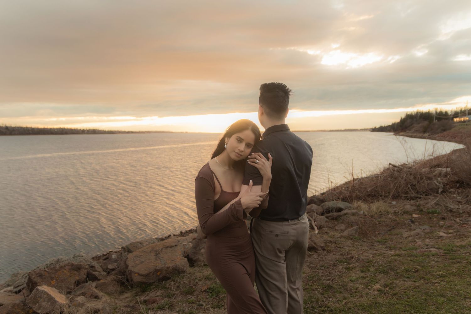 Couple embracing on rocky coastline during sunset.