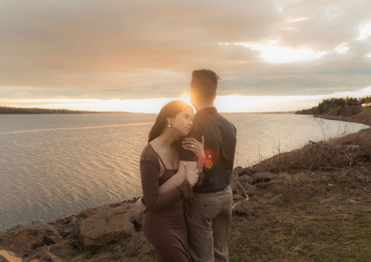 Romantic sunset moment by the water as couple stands on rocky shore.