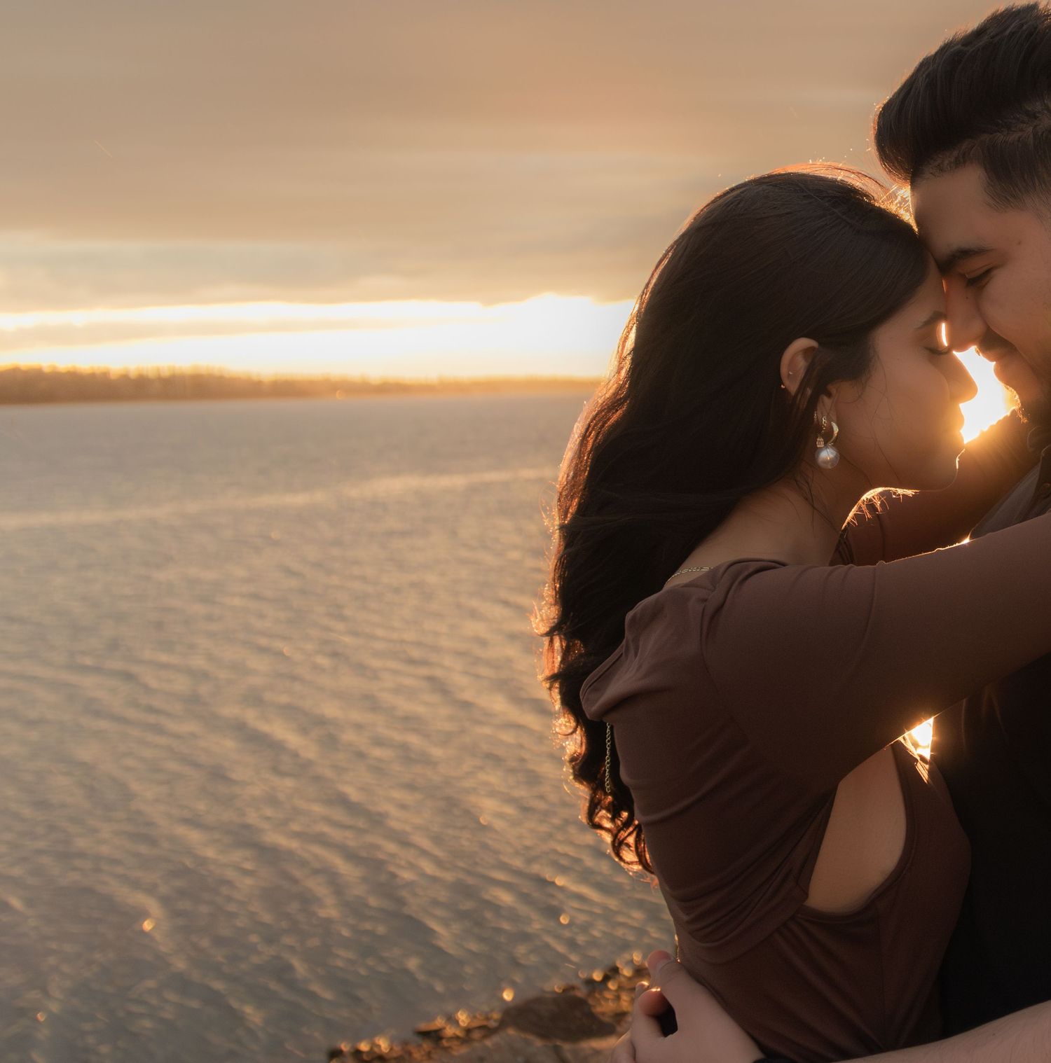 Silhouetted couple embracing against golden sunset over water.