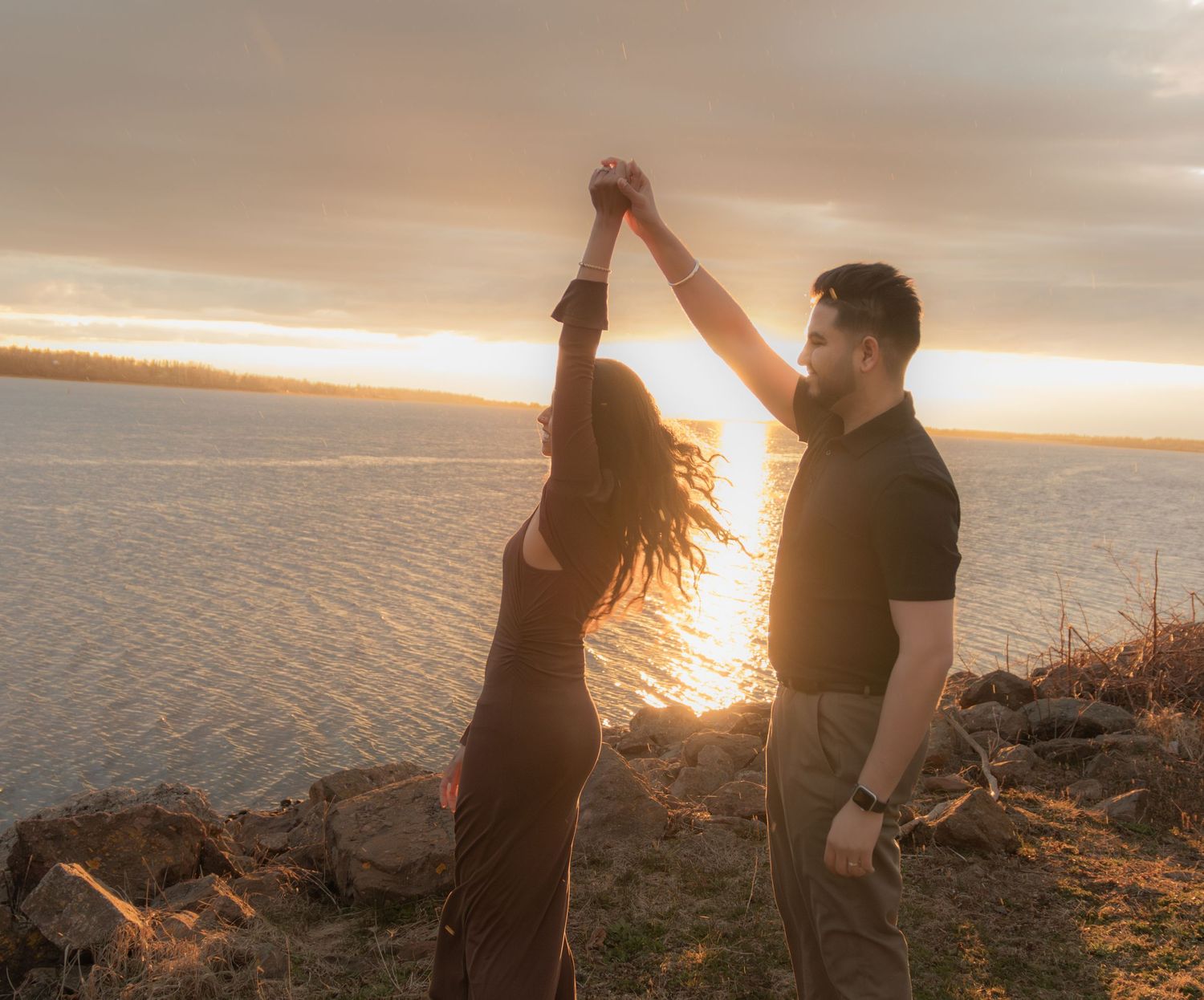 Dancing couple silhouetted against sunset sky by the ocean.