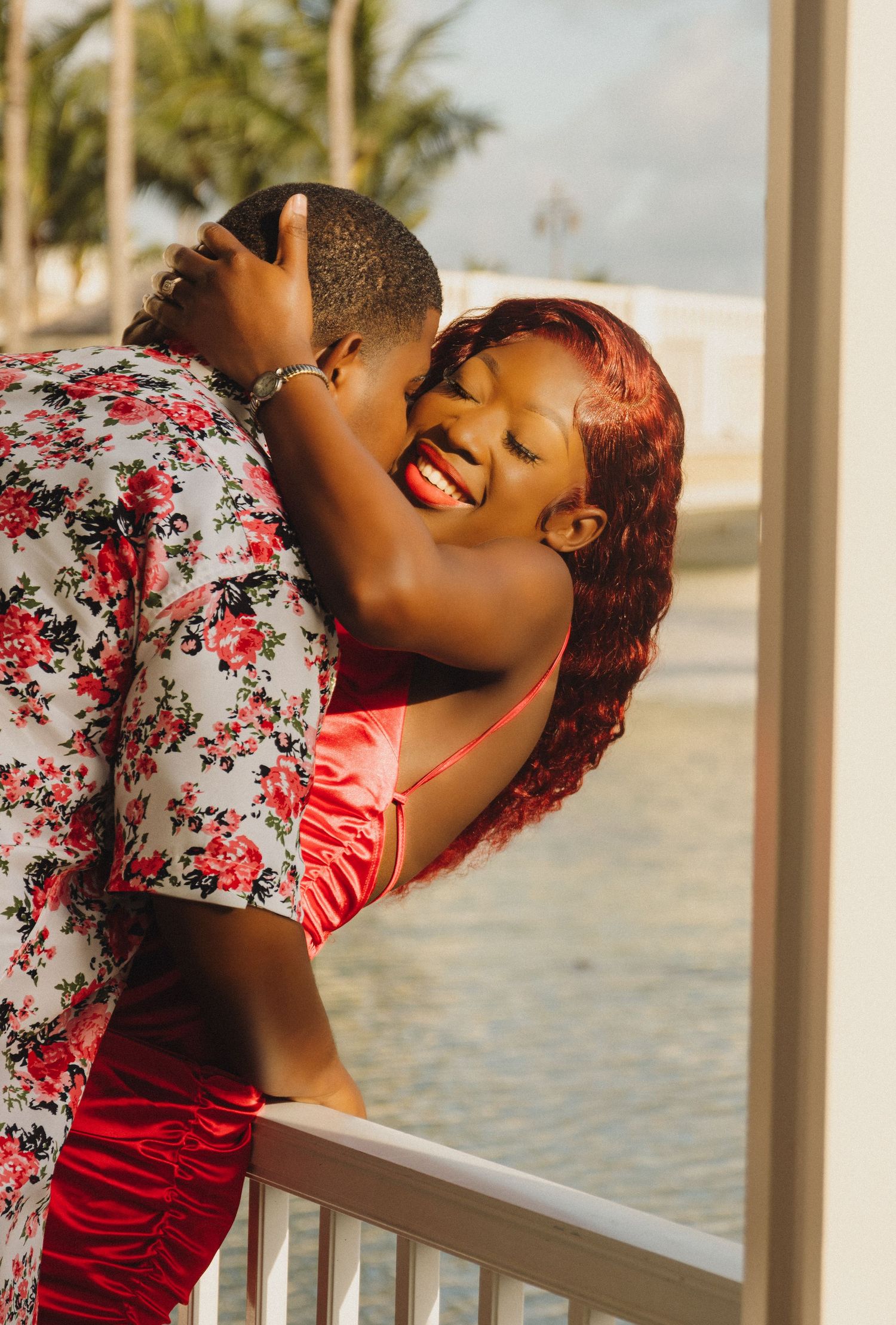 Couple shares an intimate moment on a waterfront balcony during sunset.