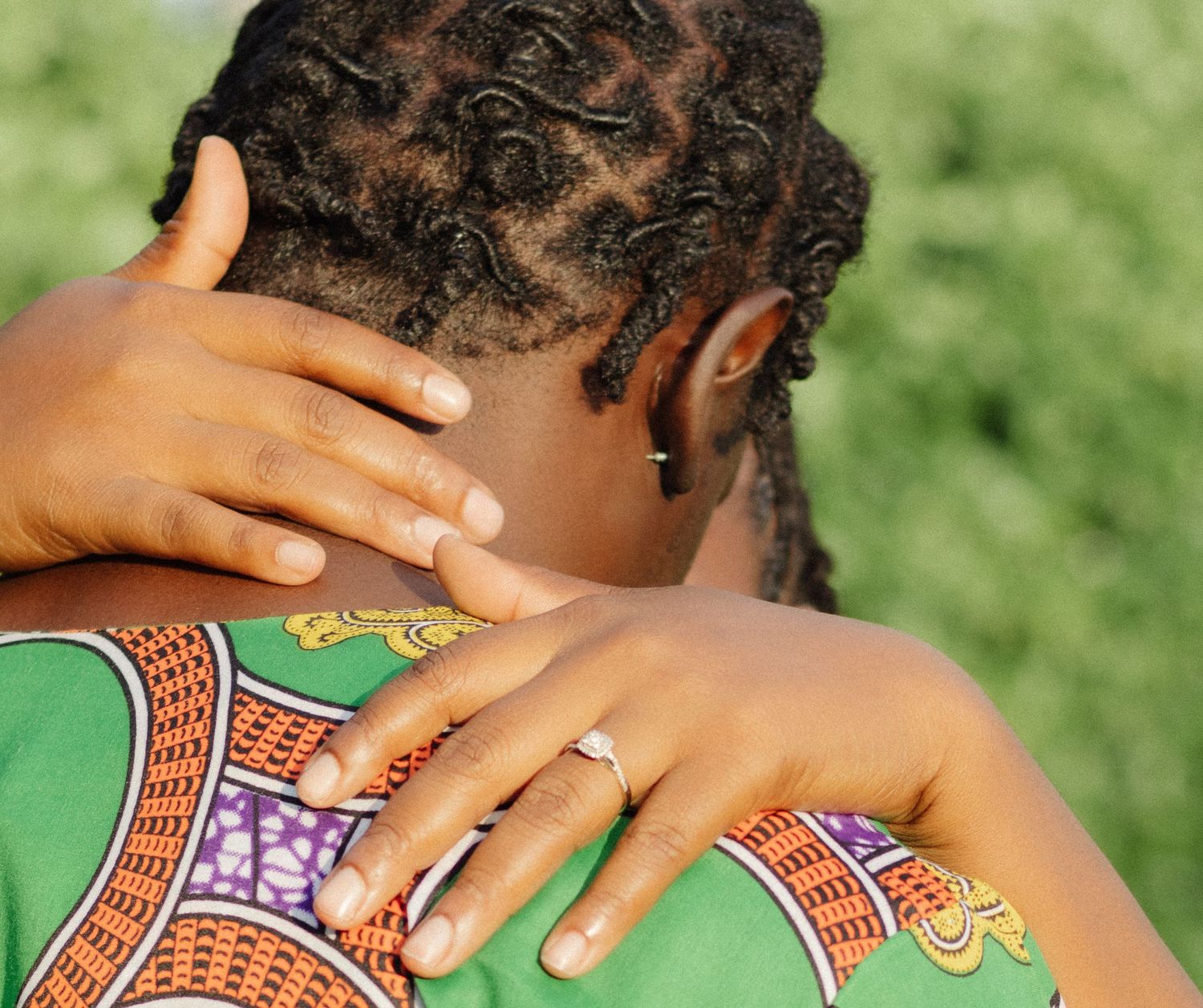 Close-up of hands displaying engagement ring on person wearing African print fabric.