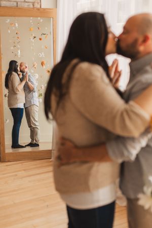A couple embraces in front of a mirror with flower decorations hanging on the wall behind them.