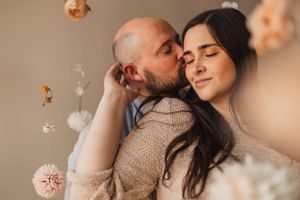 Romantic couple in warm neutral tones embracing in intimate moment with soft lighting and floral elements.
