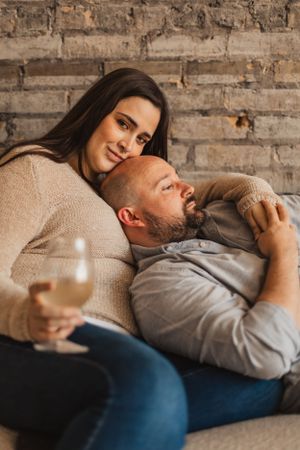 Couple relaxing together on couch with wine glass, sharing intimate moment against exposed brick wall.