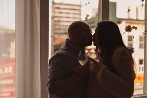 A silhouette of a couple together in front of large windows during sunset.