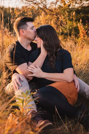 Romantic couple sharing an intimate moment of one kissing the other on the forehead in golden sunlit field during sunset.