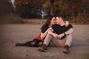 Couple sitting together on the beach sand during autumn sunset creating romantic silhouettes in warm lighting.