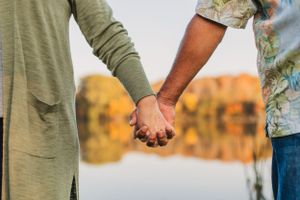 Close up shot of two hands holding each other against an autumn nature backdrop at sunset.