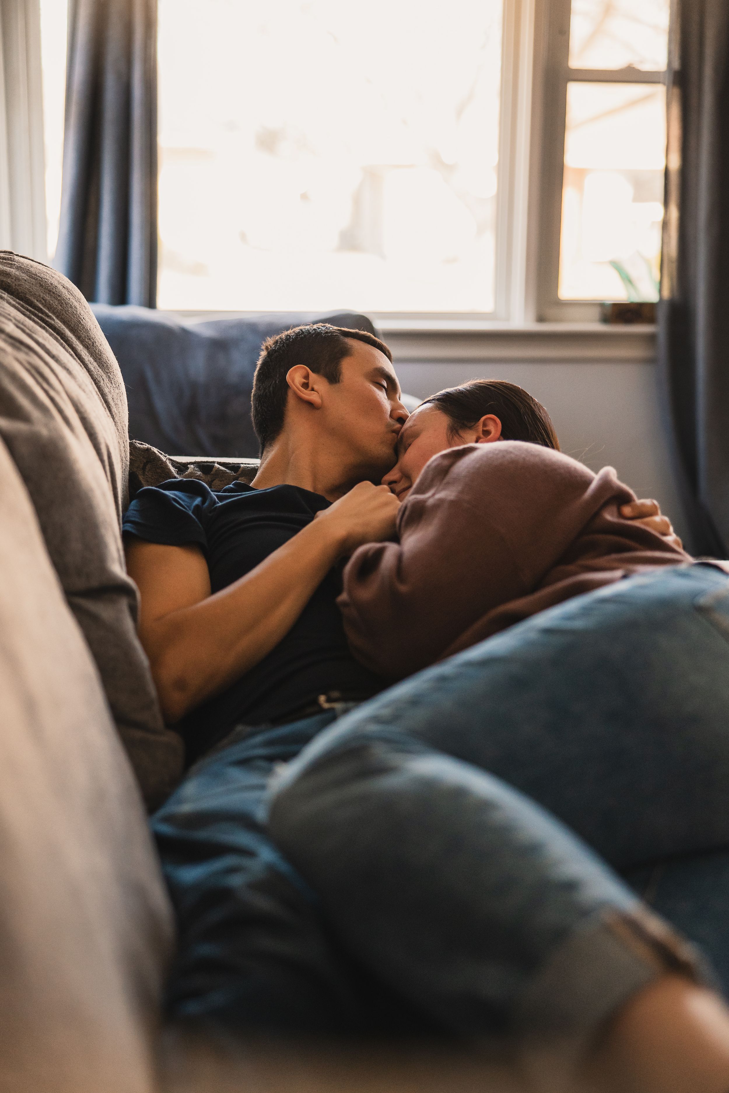 Couple resting peacefully on a couch snuggled together in their living room under natural window light.