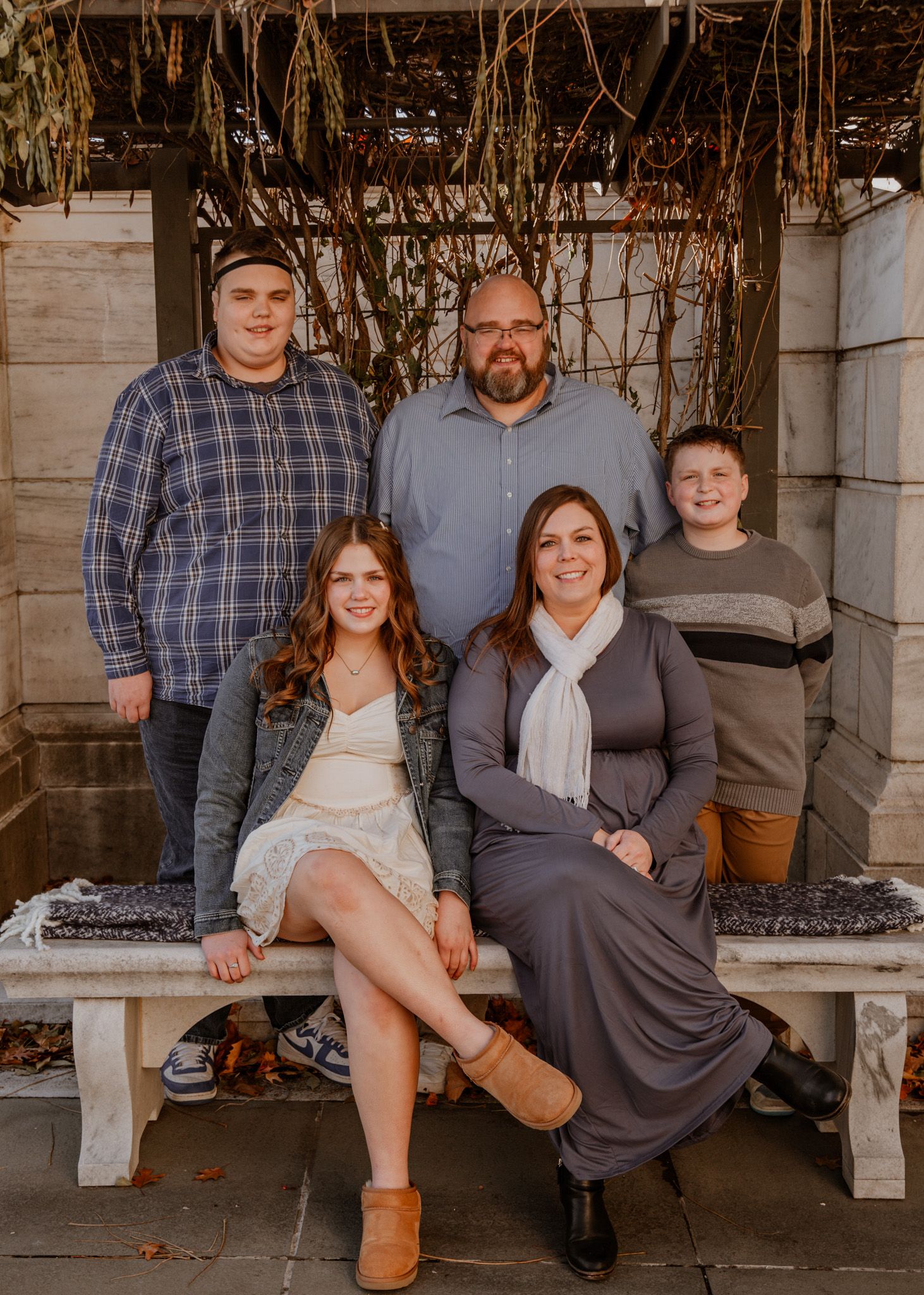 Family group photo on rustic white bench with autumn decor and natural lighting.