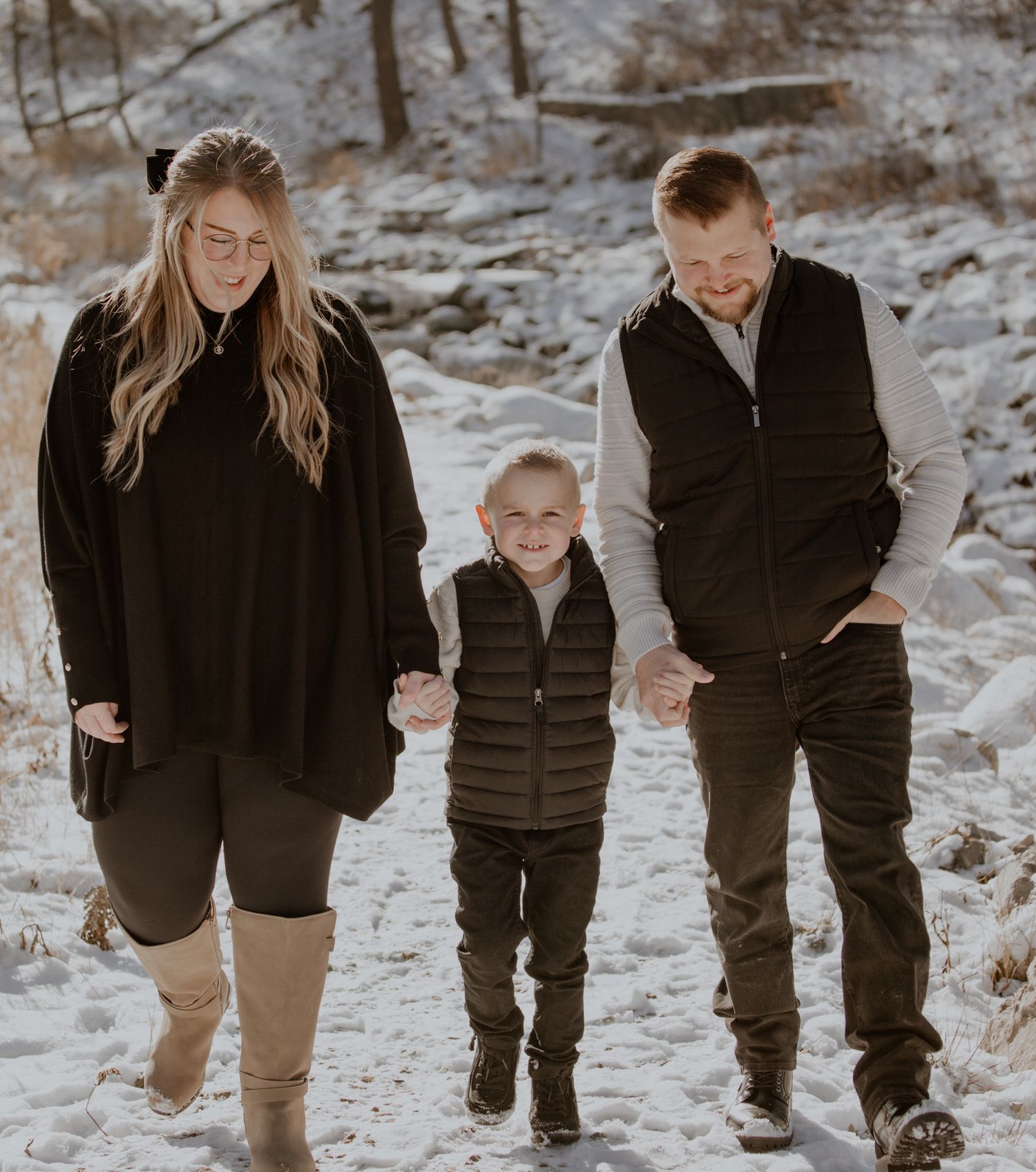 Family walking together through snowy forest path in winter attire.
