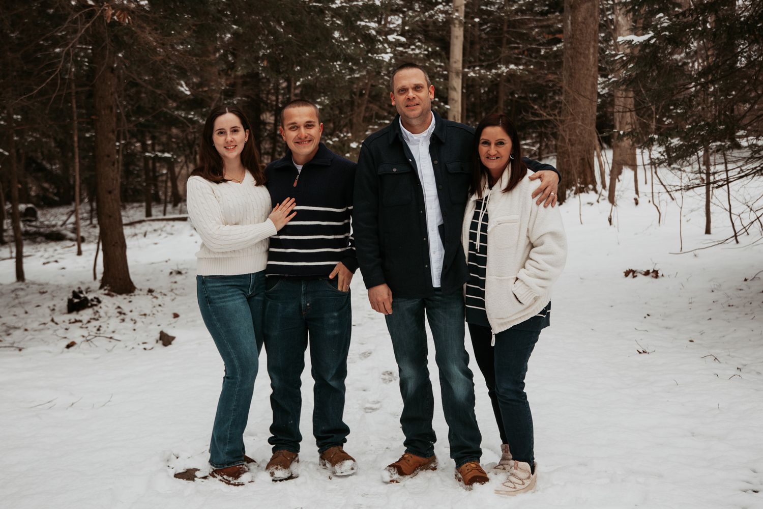 Five people pose together in a winter forest setting wearing casual clothing.