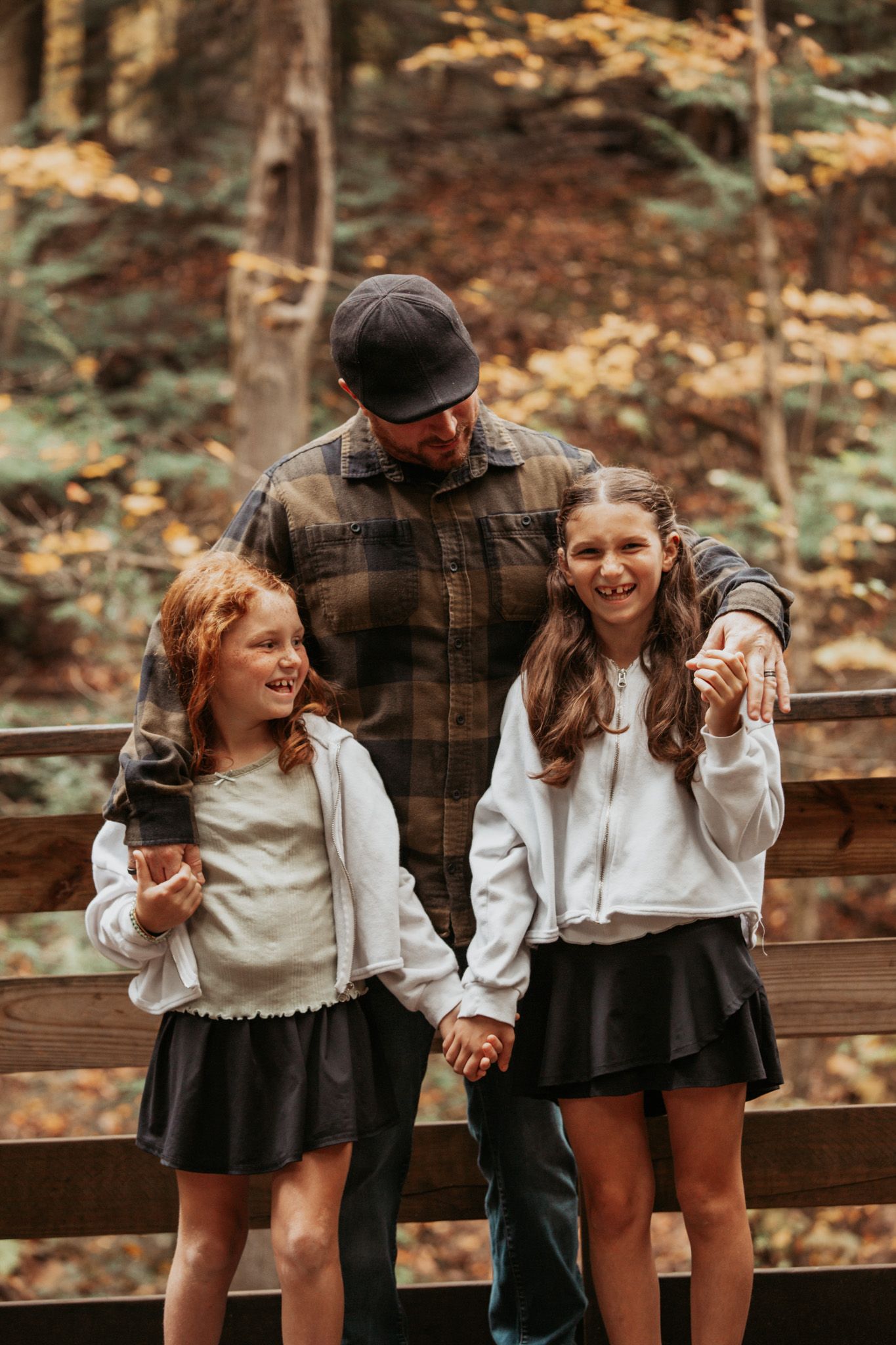 Candid family moment on wooden deck stairs surrounded by autumn trees.