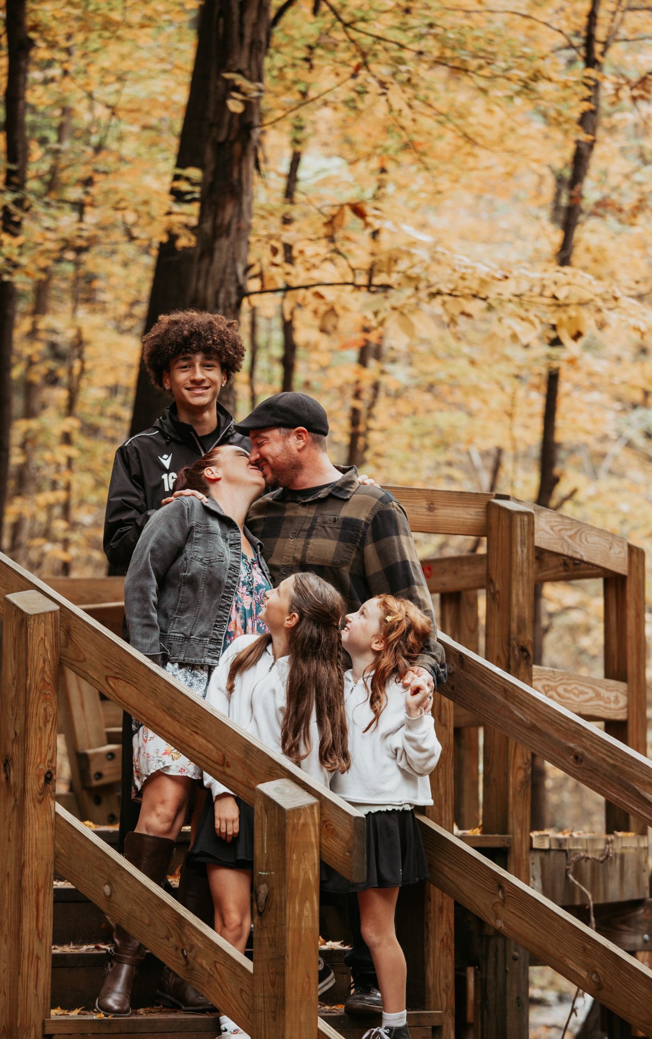 Family portrait on wooden stairs in autumn forest with fall foliage in background.