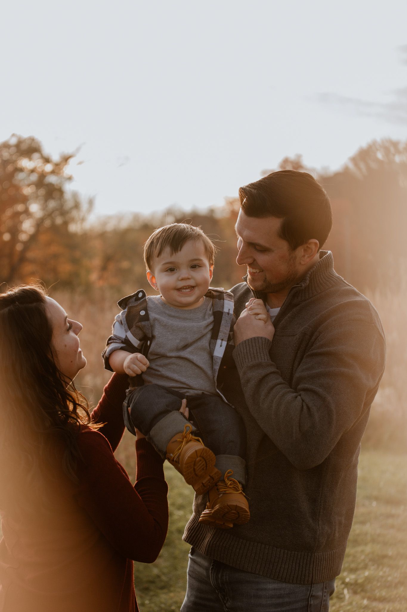 Family enjoying tender moments together during golden hour sunset photoshoot in a field.