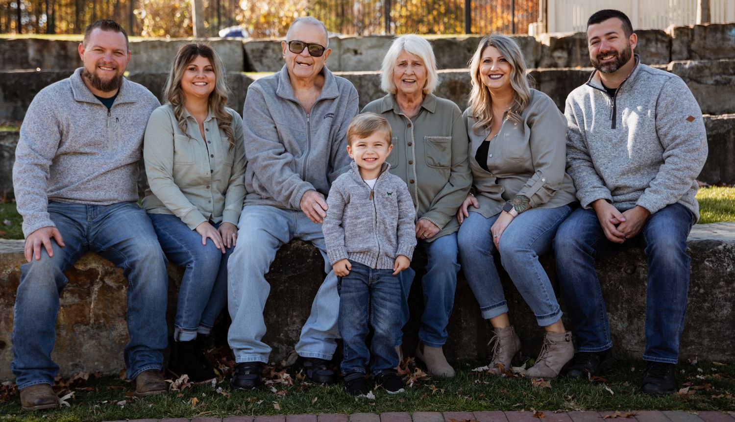 Extended family members pose together on a stone wall during an autumn photoshoot.
