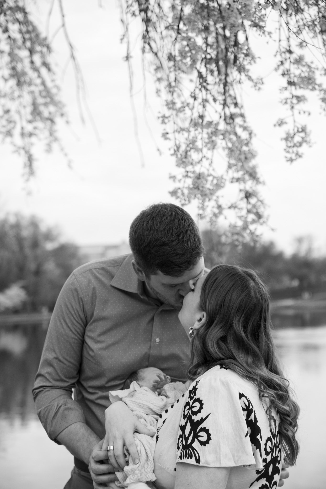 A romantic couple shares tender moments outdoors near a lake in black and white.