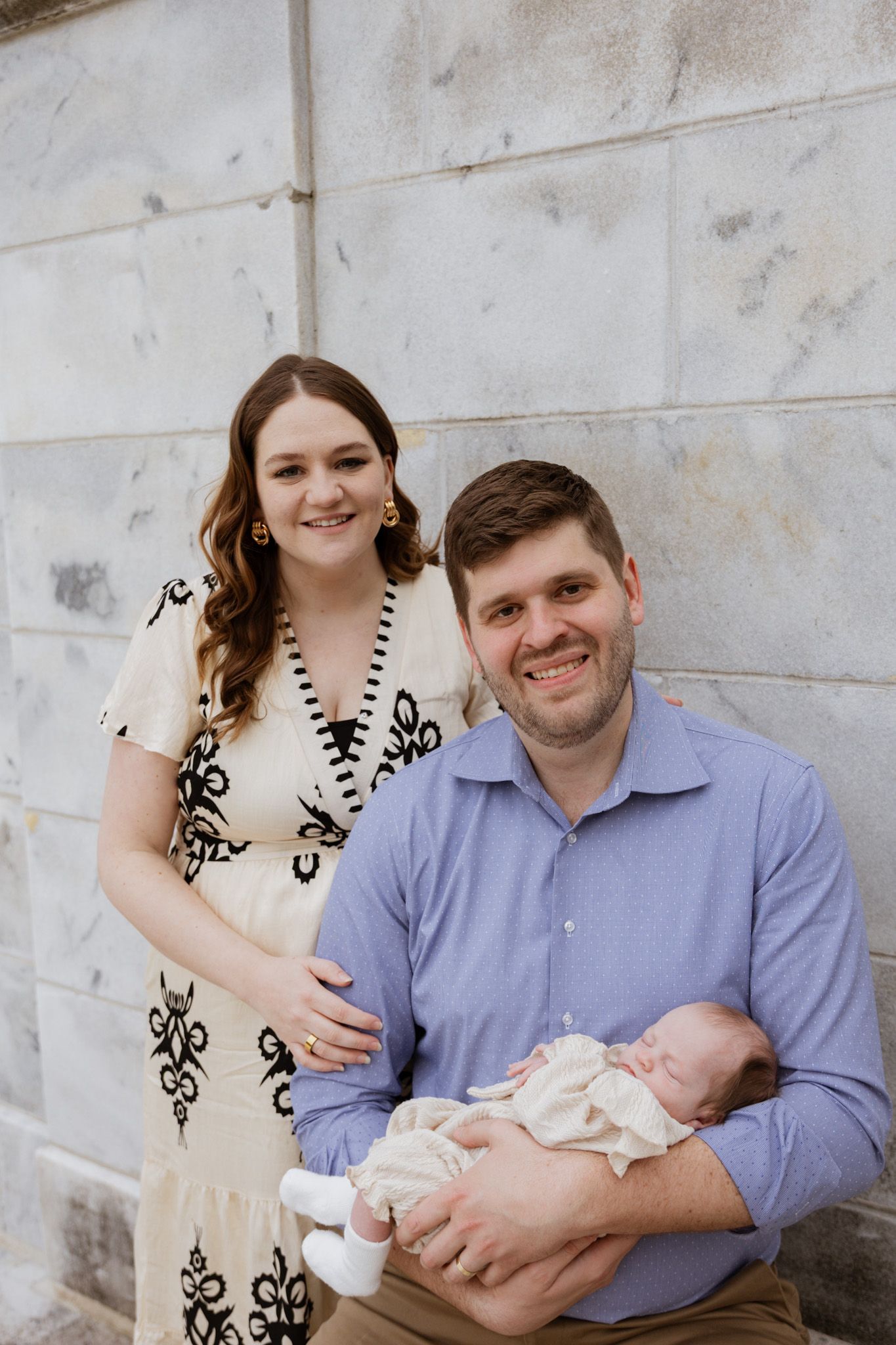 A family portrait with a newborn baby against a white wall background.
