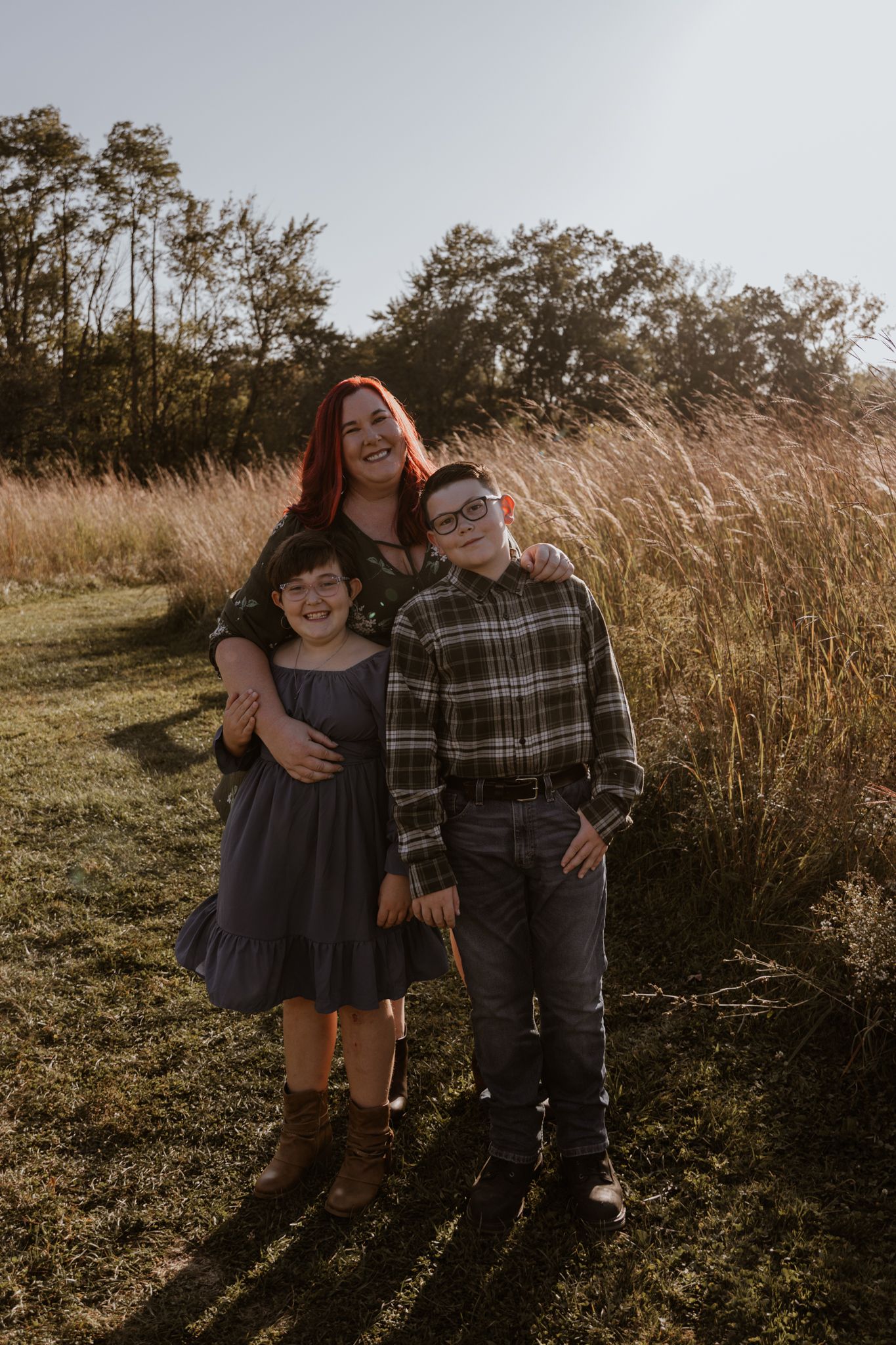 A couple poses together in a field of tall grass during a golden hour photoshoot.