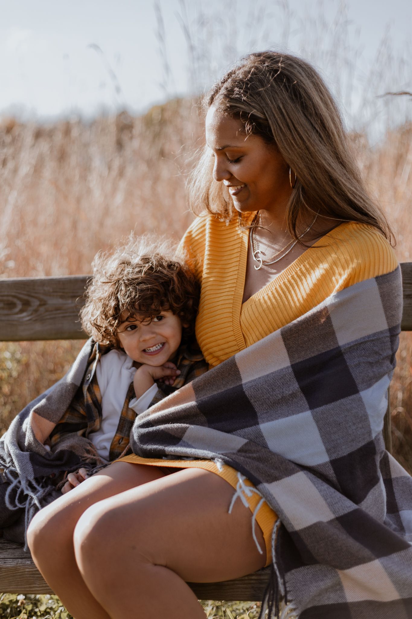 Family cuddles under cozy blanket during autumn outdoor photoshoot.