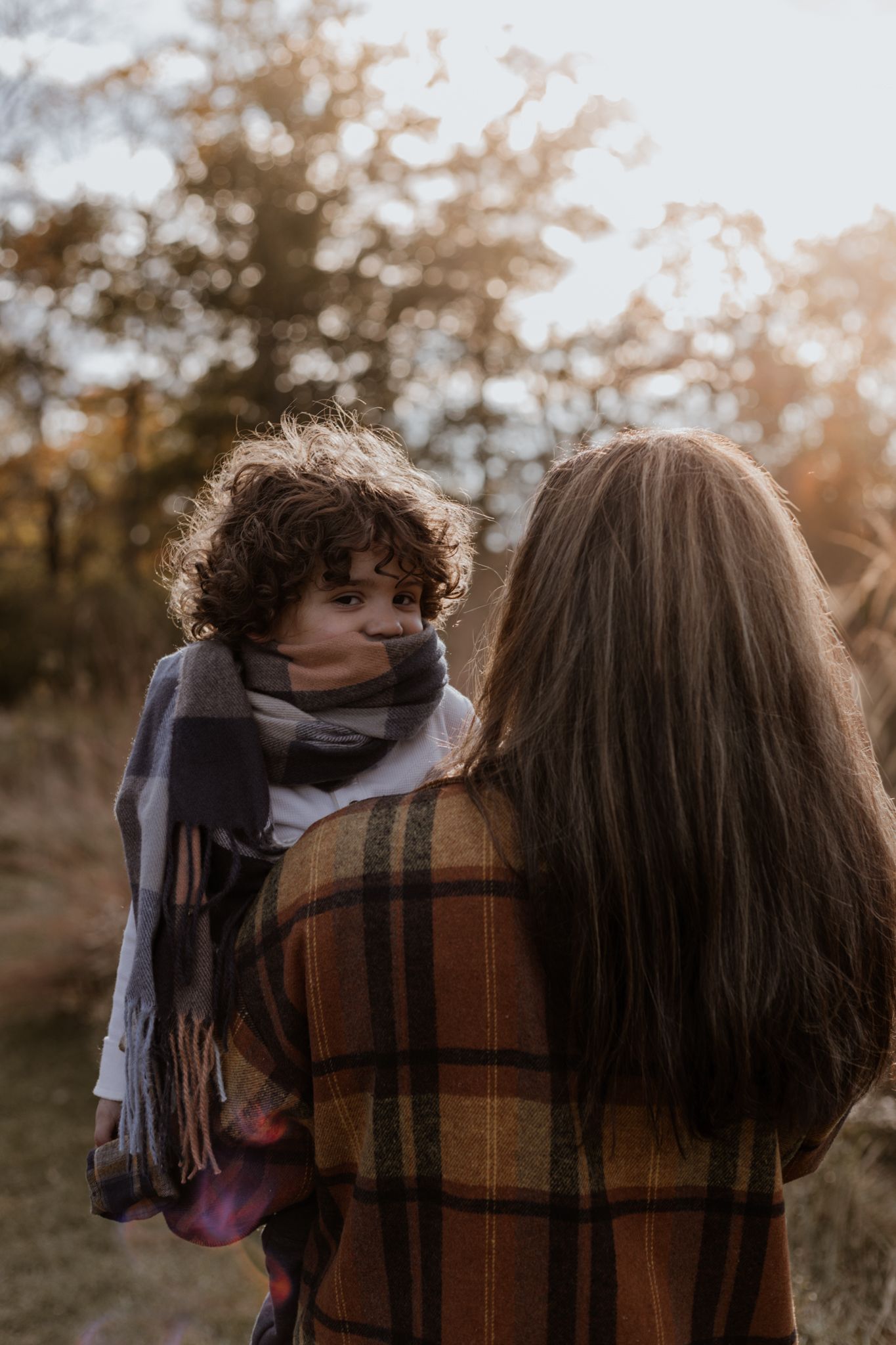 Mother and child share playful moments in autumn setting with plaid blanket.