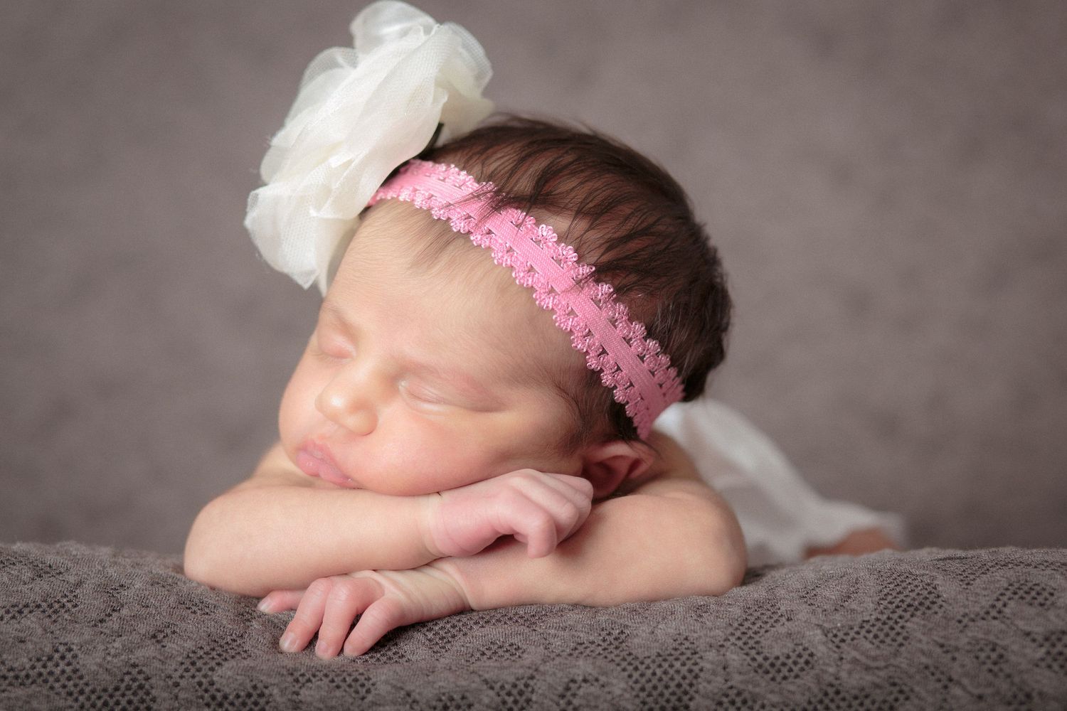 Newborn baby asleep with flower bow on her head and folded arms. She is asleep photo by Eternity Fine Portraits